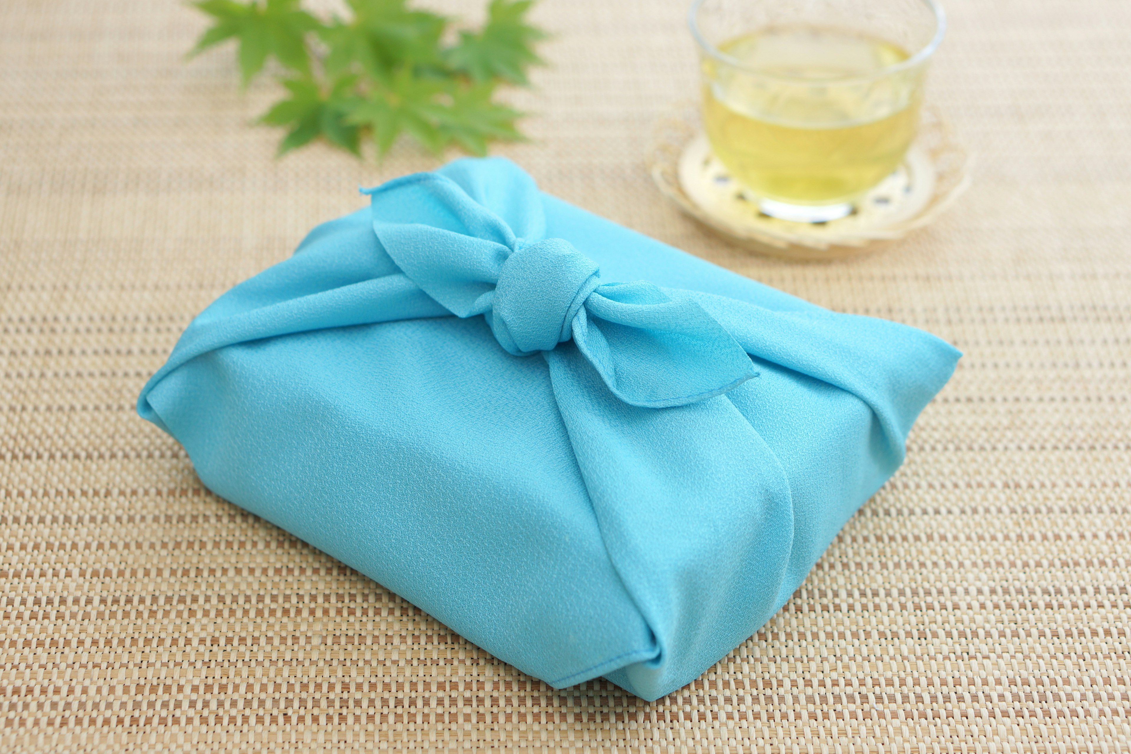 A gift wrapped in blue fabric with green leaves and a cup of tea