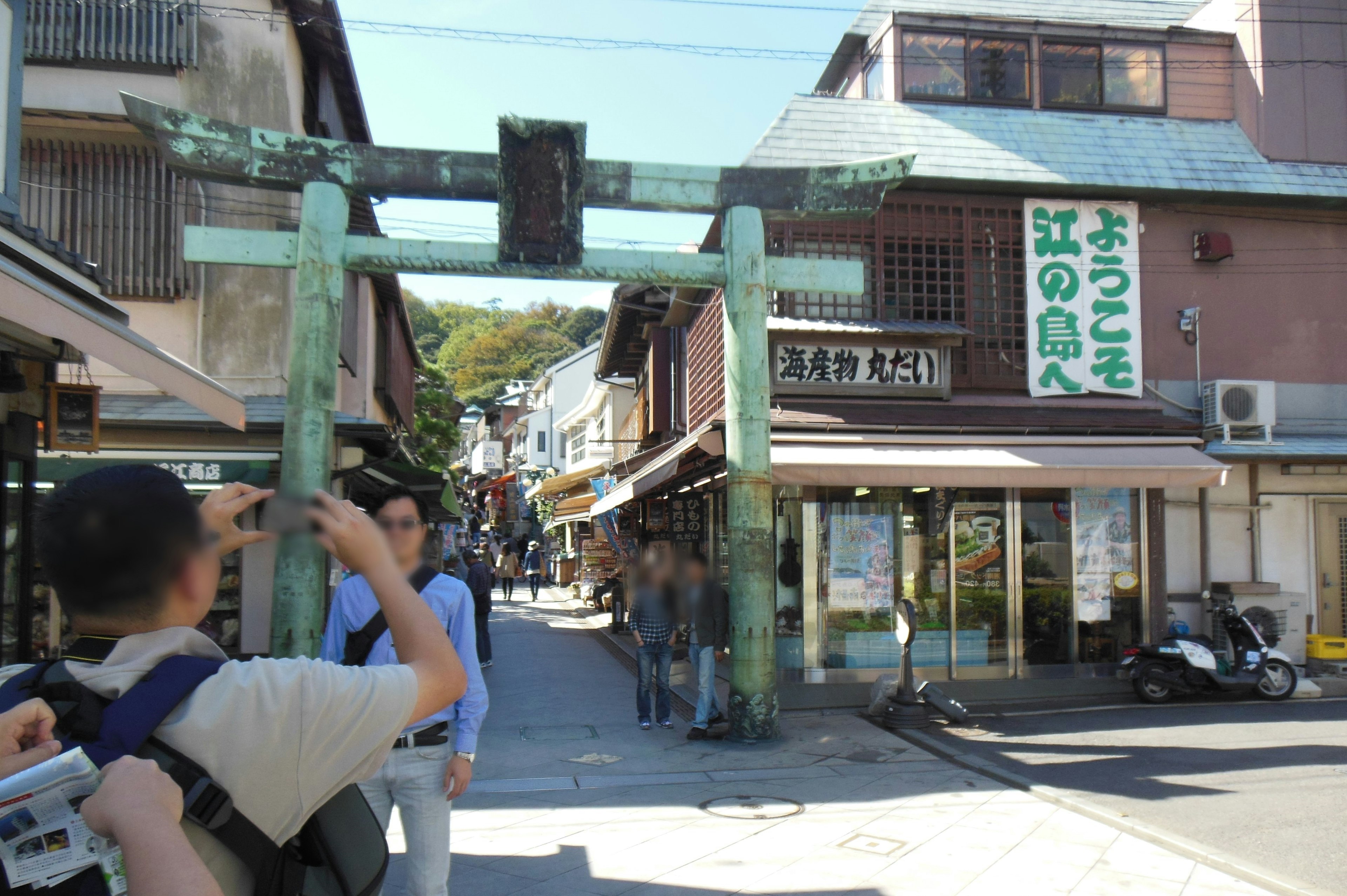 青銅の鳥居と賑やかな商店街の風景