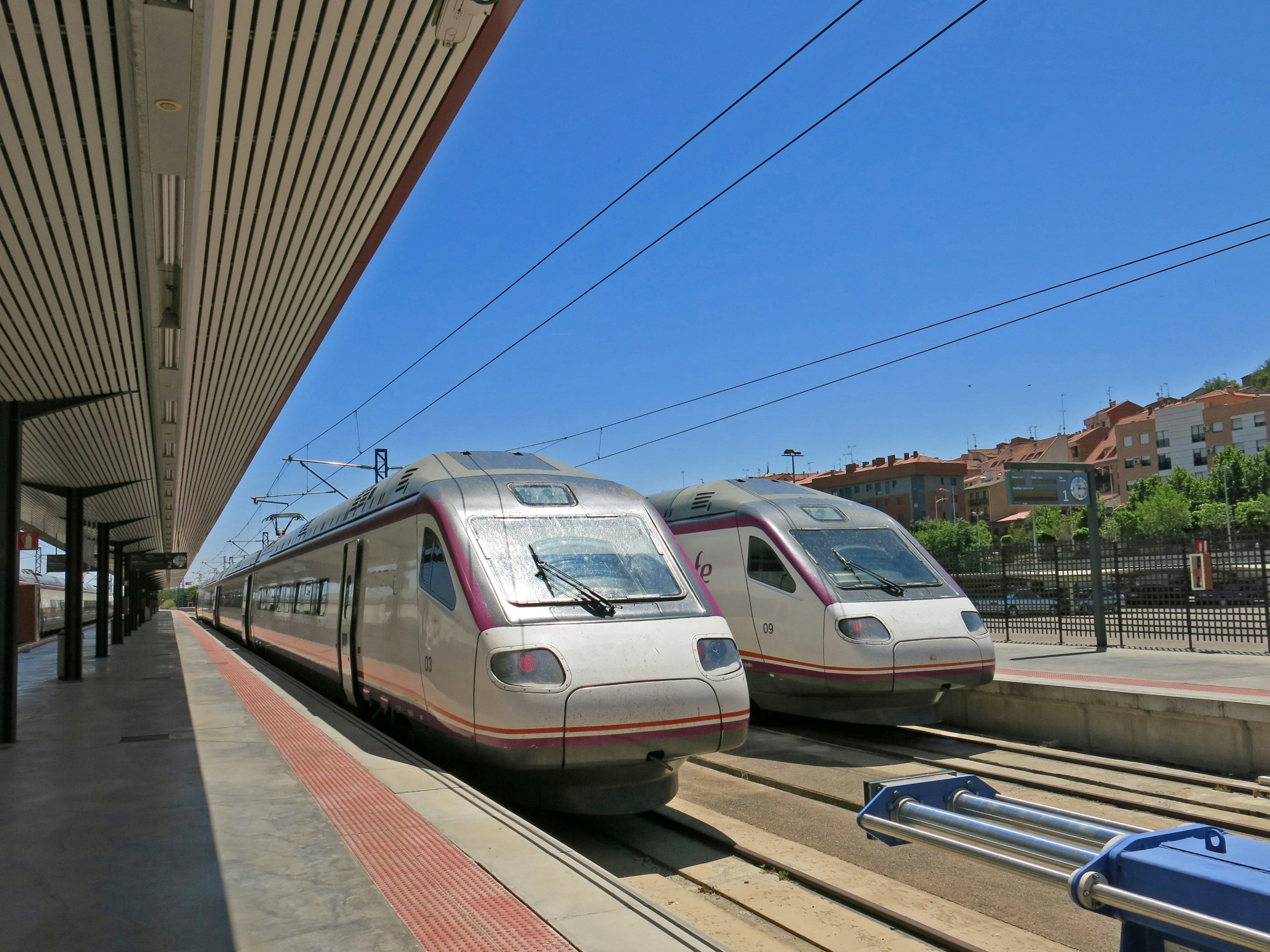 Dos trenes detenidos en una estación bajo un cielo azul brillante