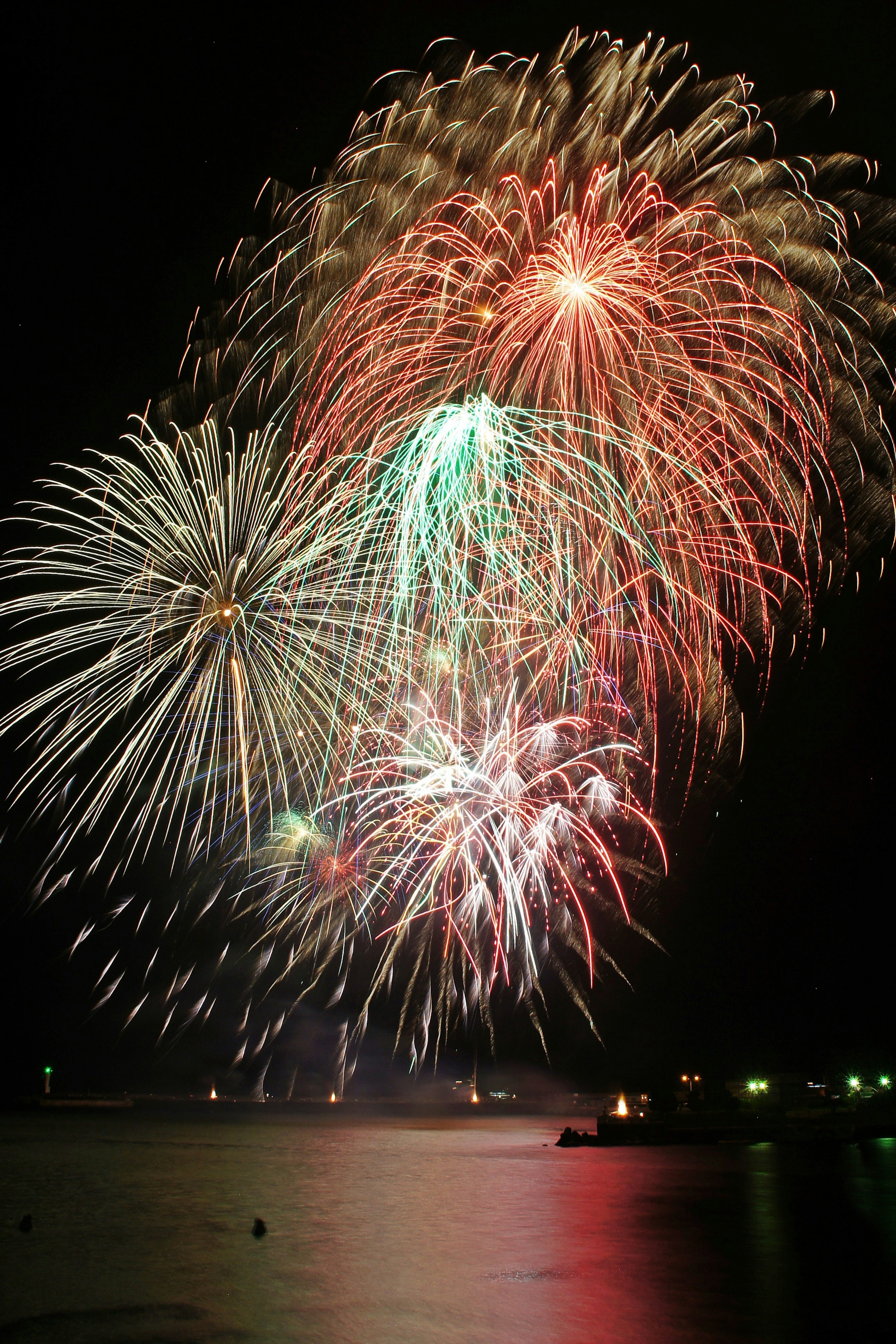 Colorful fireworks bursting in the night sky over a reflective water surface