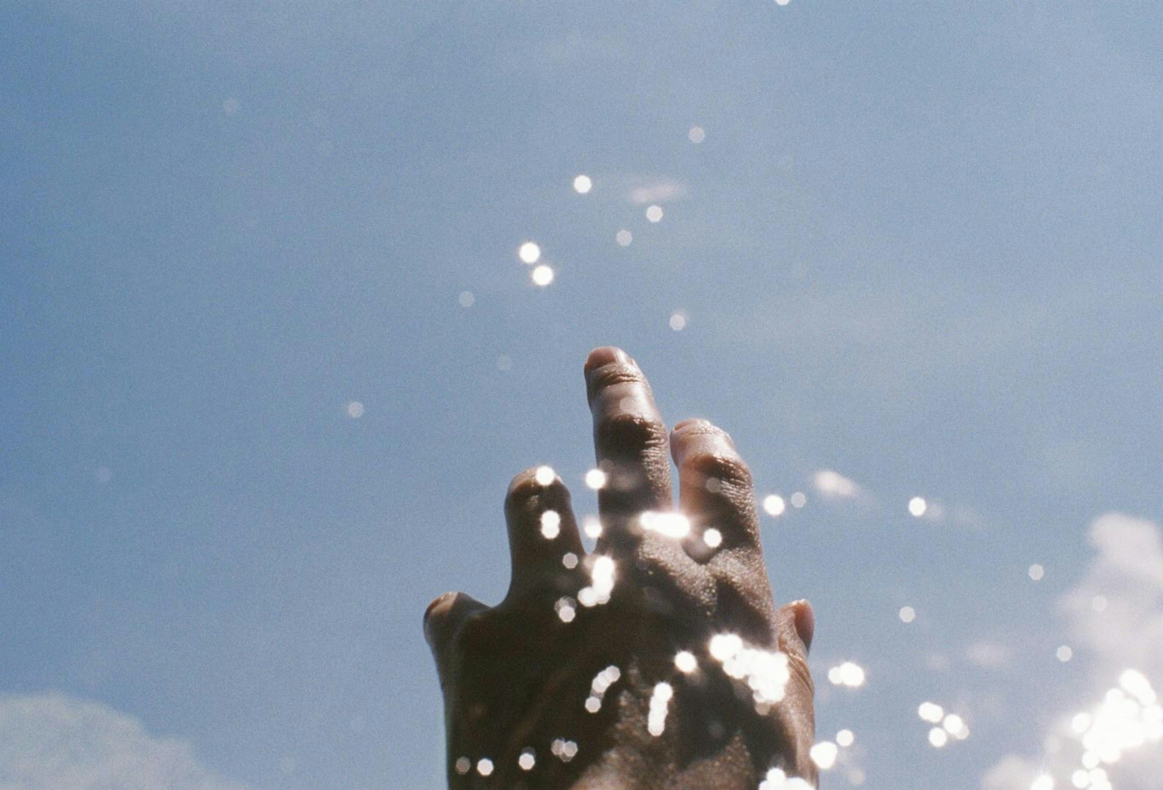 Hand reaching out surrounded by water splashes and blue sky