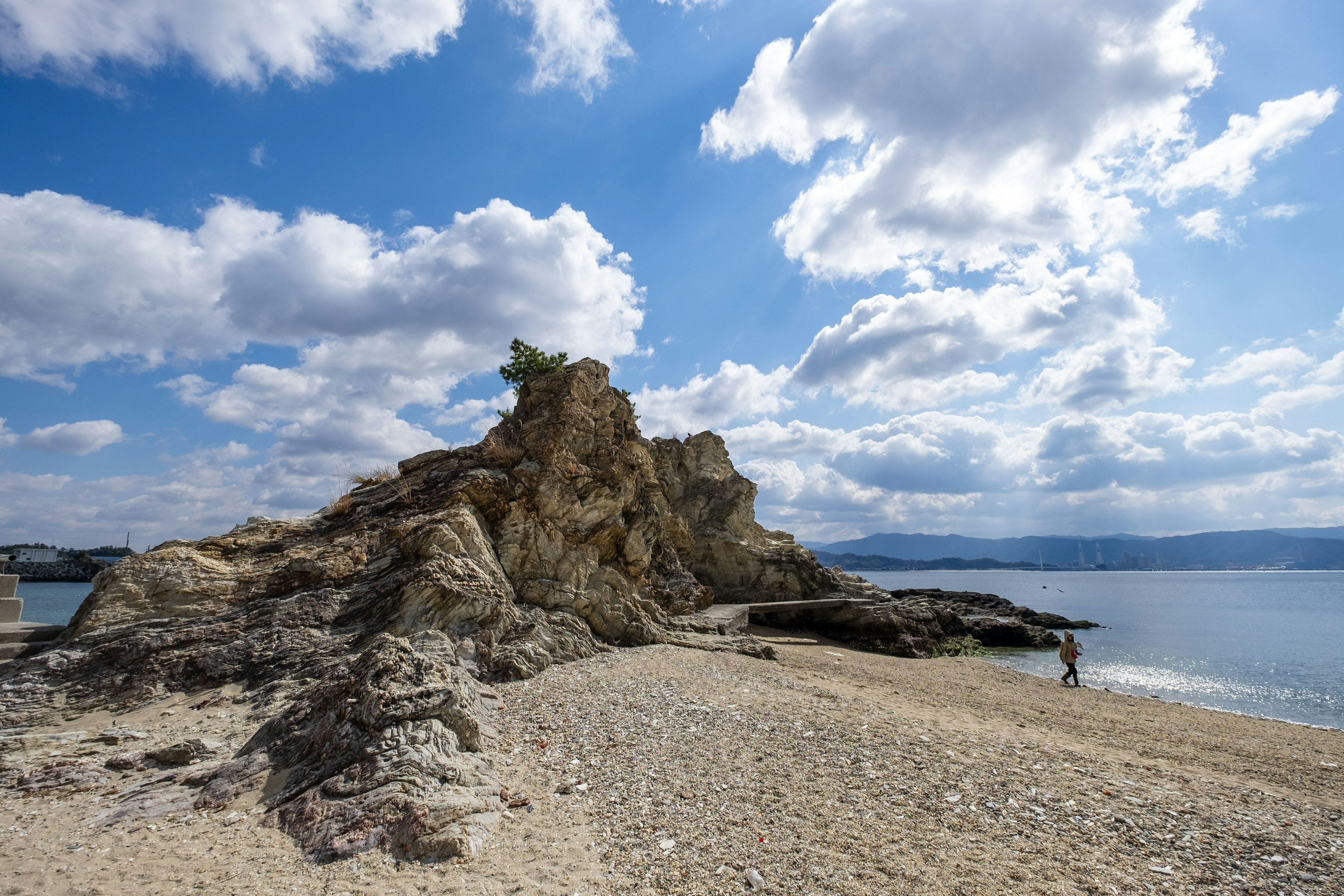 Paesaggio costiero con cielo blu e nuvole bianche che presenta una spiaggia rocciosa