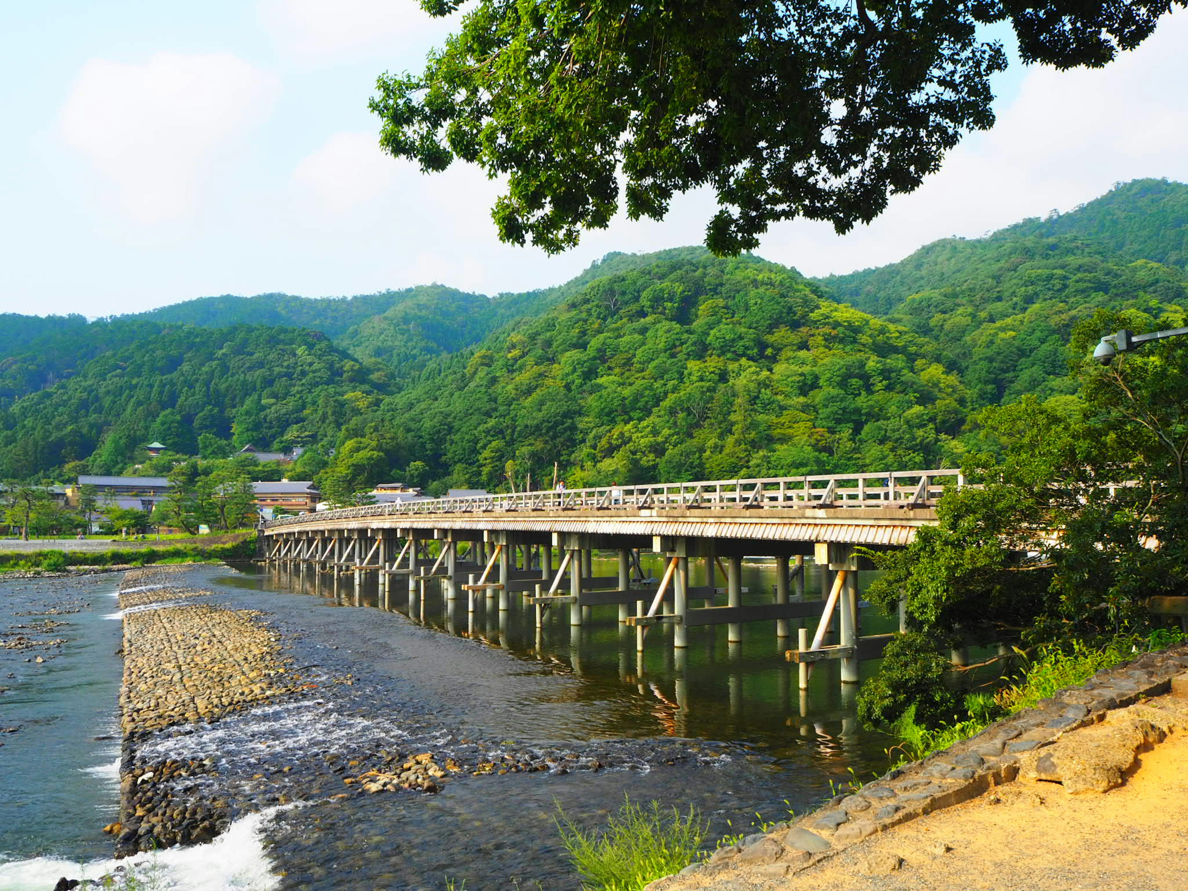 ทิวทัศน์ของสะพานไม้ข้ามแม่น้ำที่มีภูเขาเขียวขจีล้อมรอบ