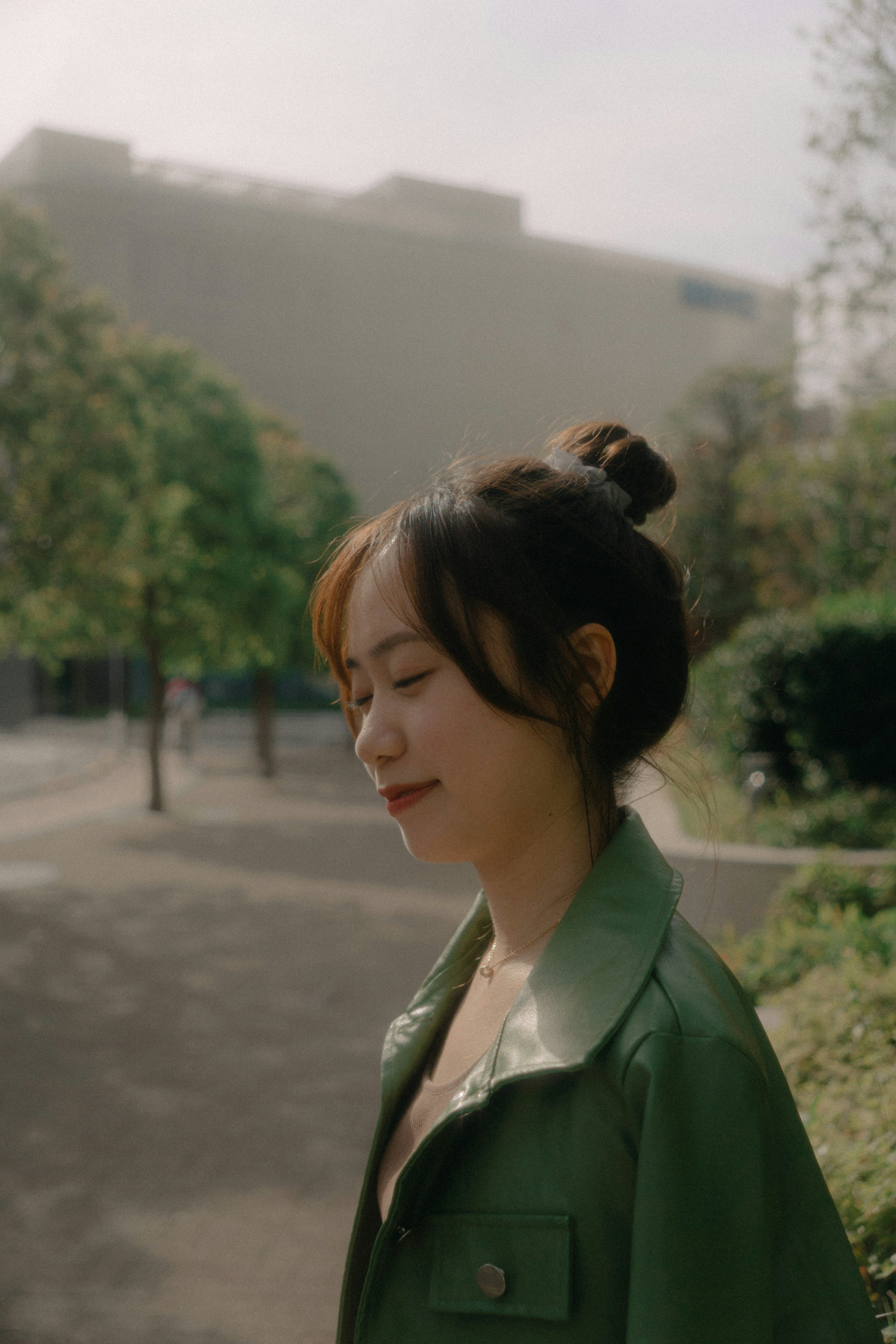 A woman in a green jacket smiling with her head turned in a park setting