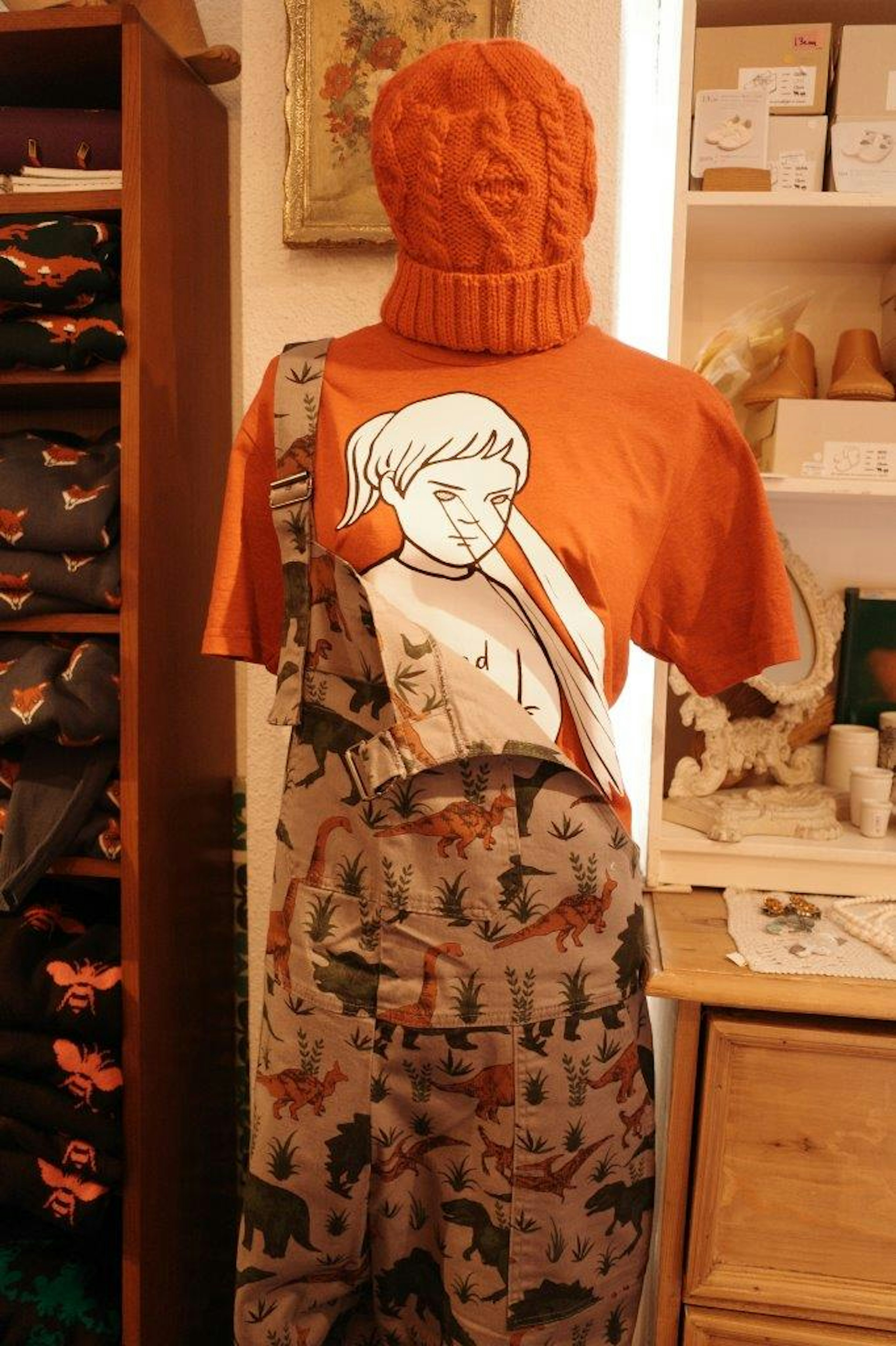 Un mannequin portant un t-shirt orange avec un design graphique et des salopettes à motifs