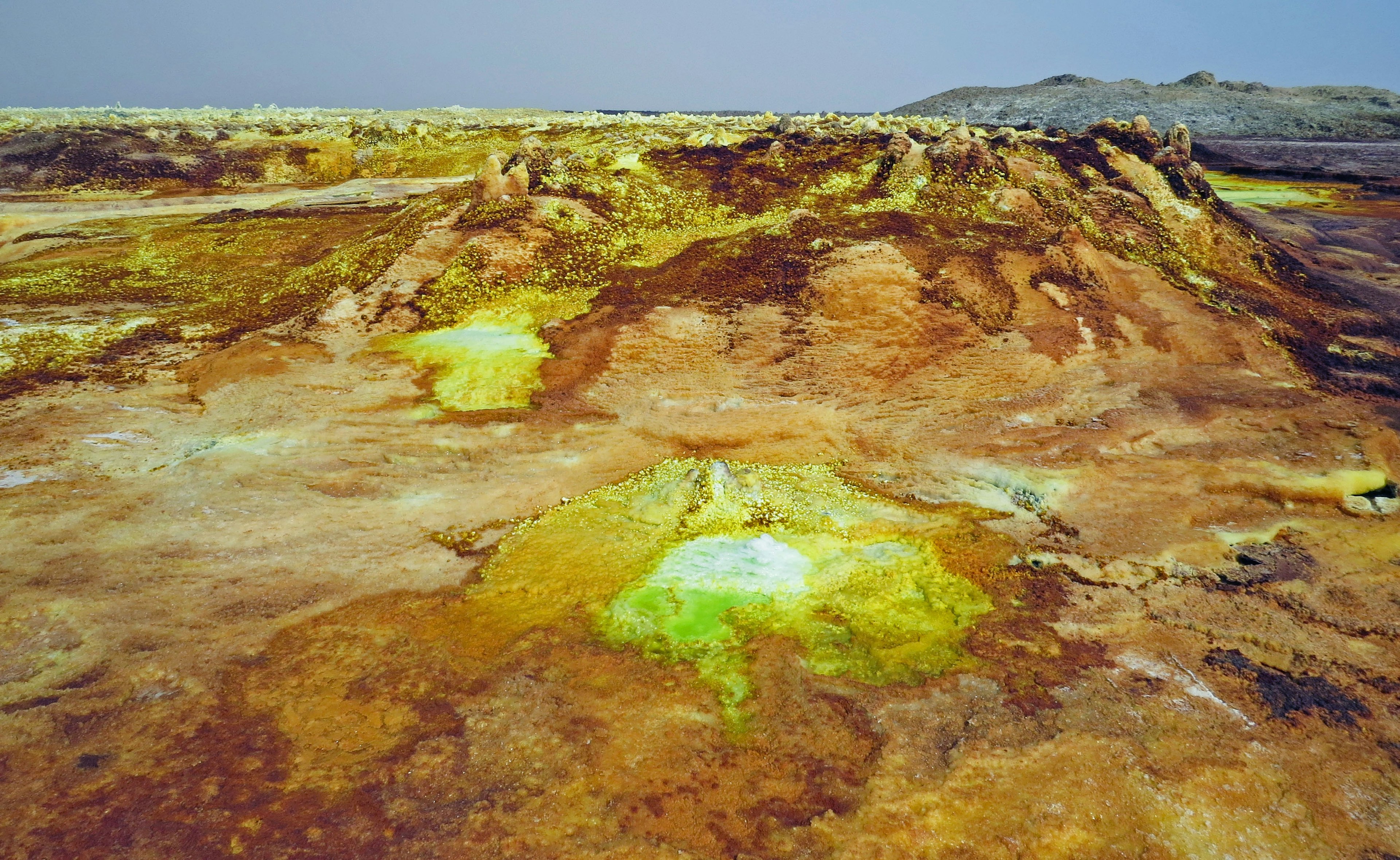 Surreale Landschaft der Danakil-Depression in Äthiopien mit gelb-grünen Schwefelablagerungen und braunem Gelände