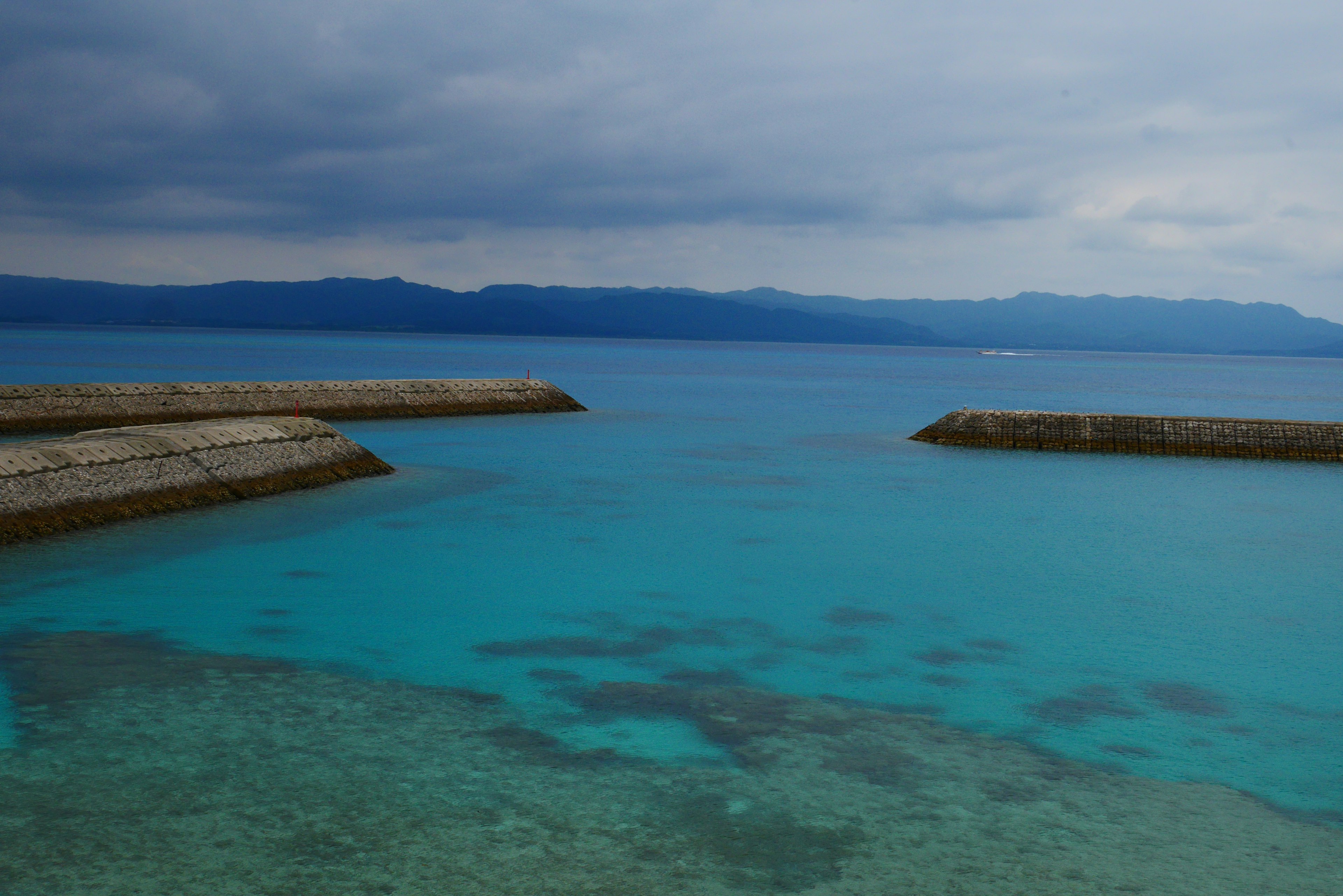 Lautan turquoise yang luas di bawah langit mendung dengan pegunungan di kejauhan