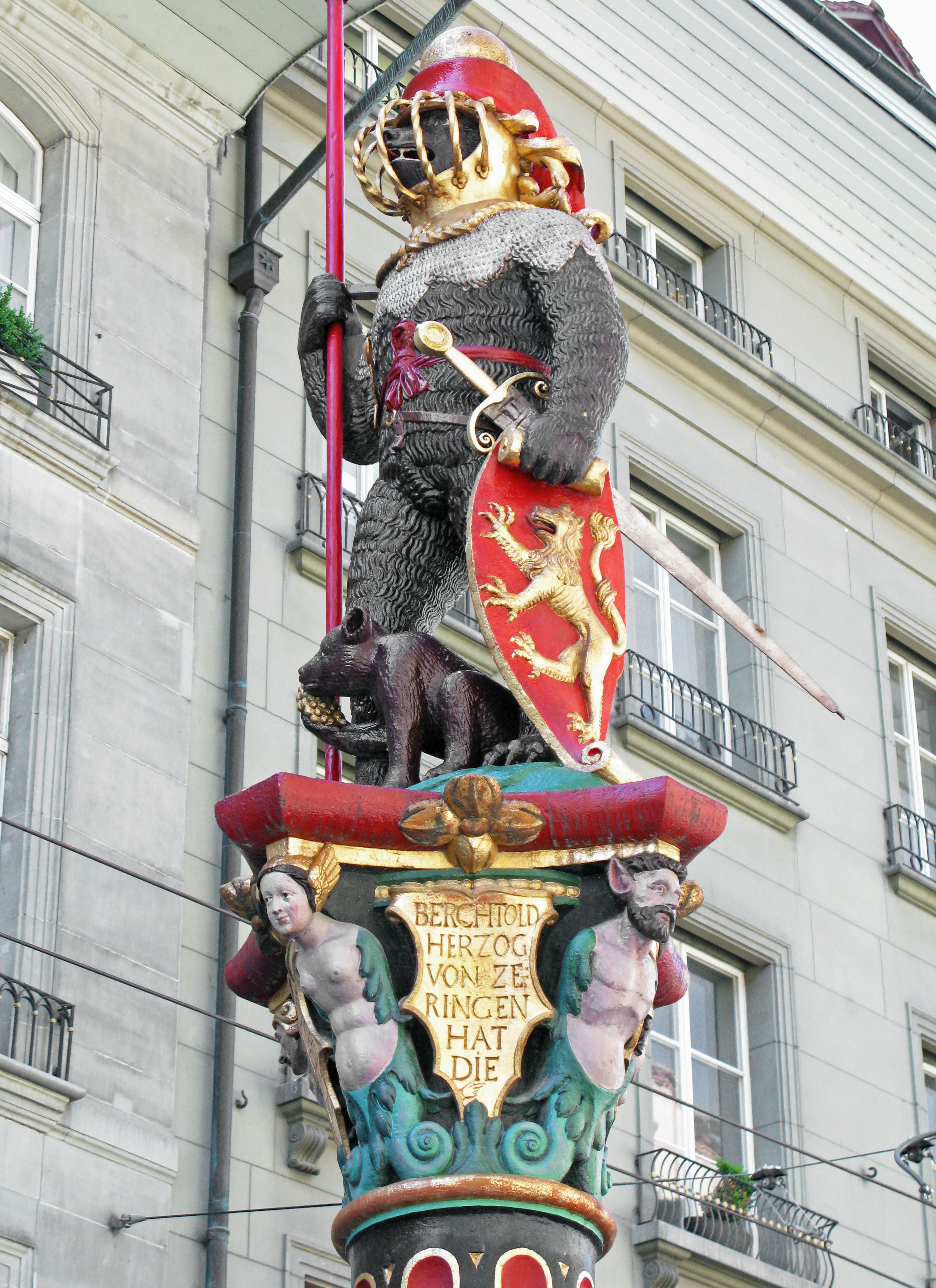 Une statue de chevalier médiéval se tenant sur une colonne colorée portant une armure tenant un bouclier rouge avec un chien aux pieds du chevalier