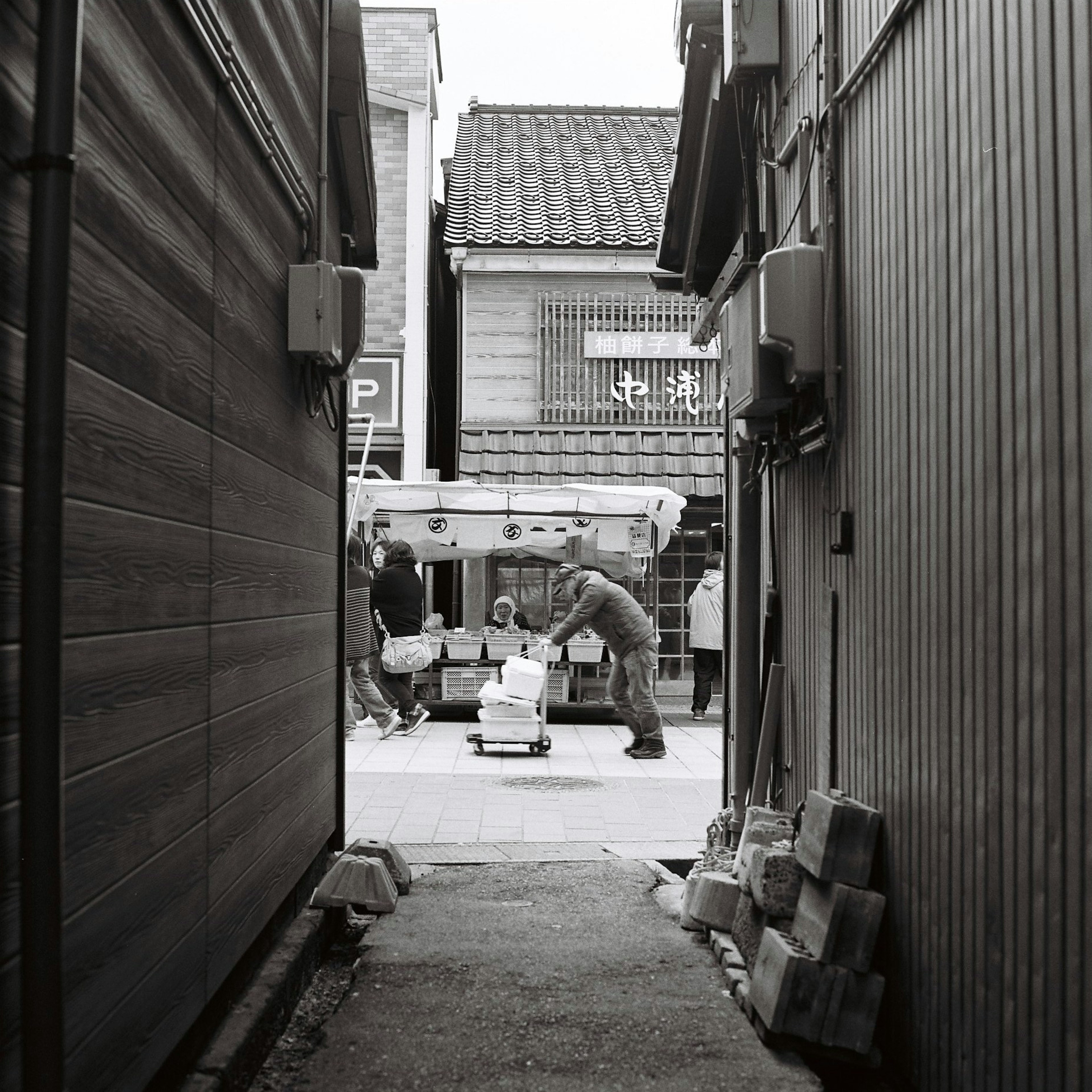 Vista de una calle comercial japonesa tradicional desde un callejón estrecho con personas transportando mercancías