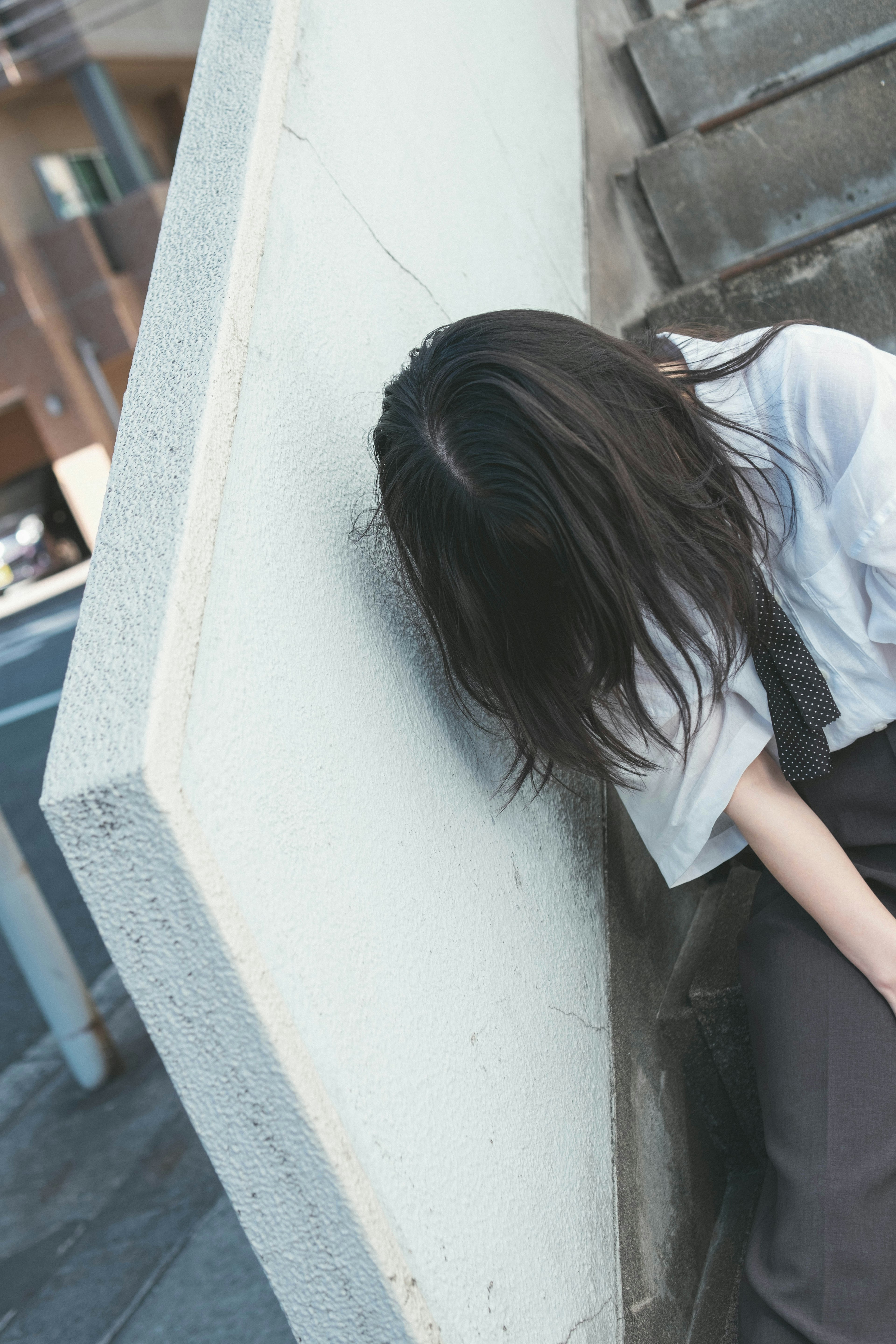 Eine Frau lehnt an einer Wand mit langen dunklen Haaren in lässiger Kleidung