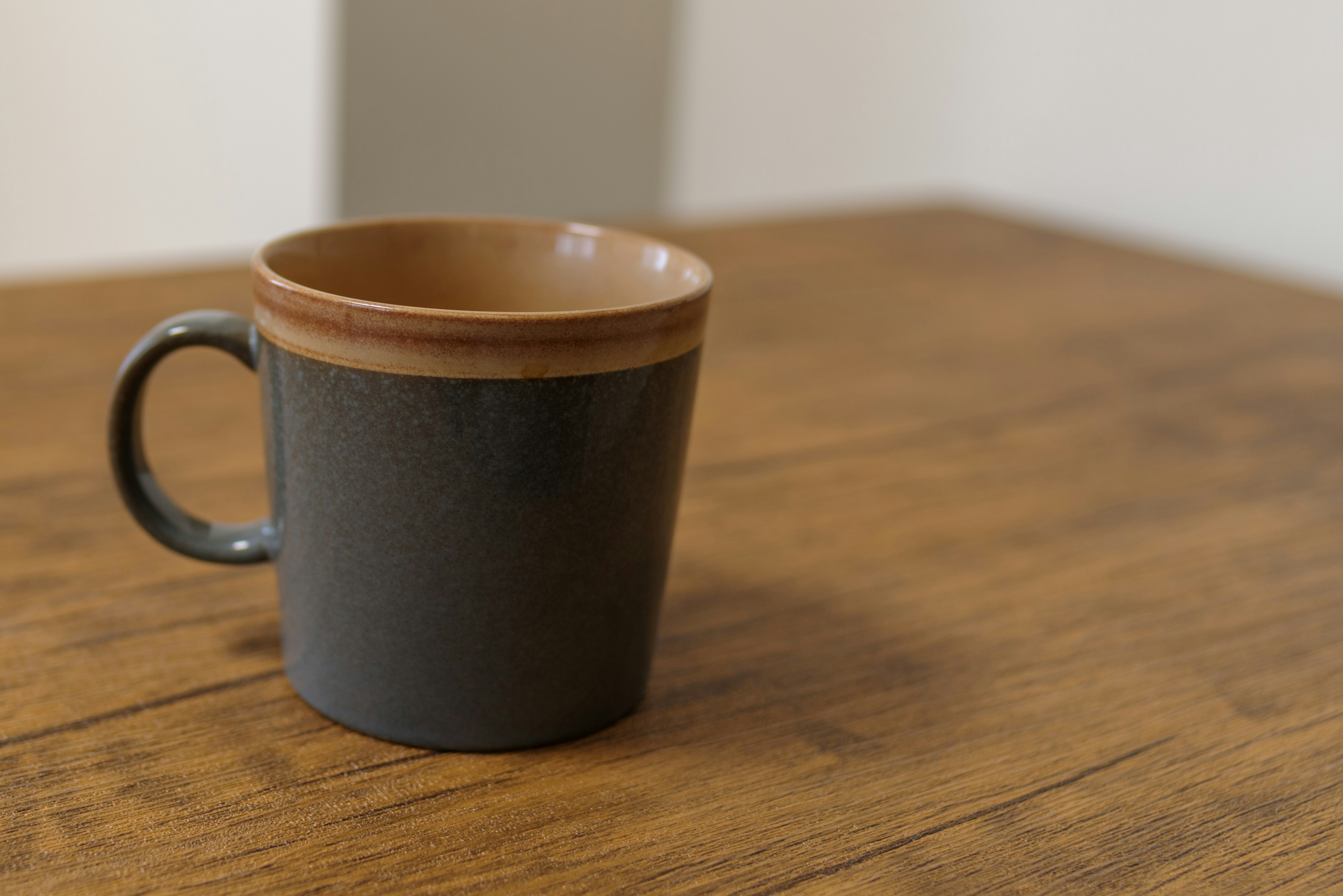 A ceramic mug with a brown interior and black exterior placed on a wooden table