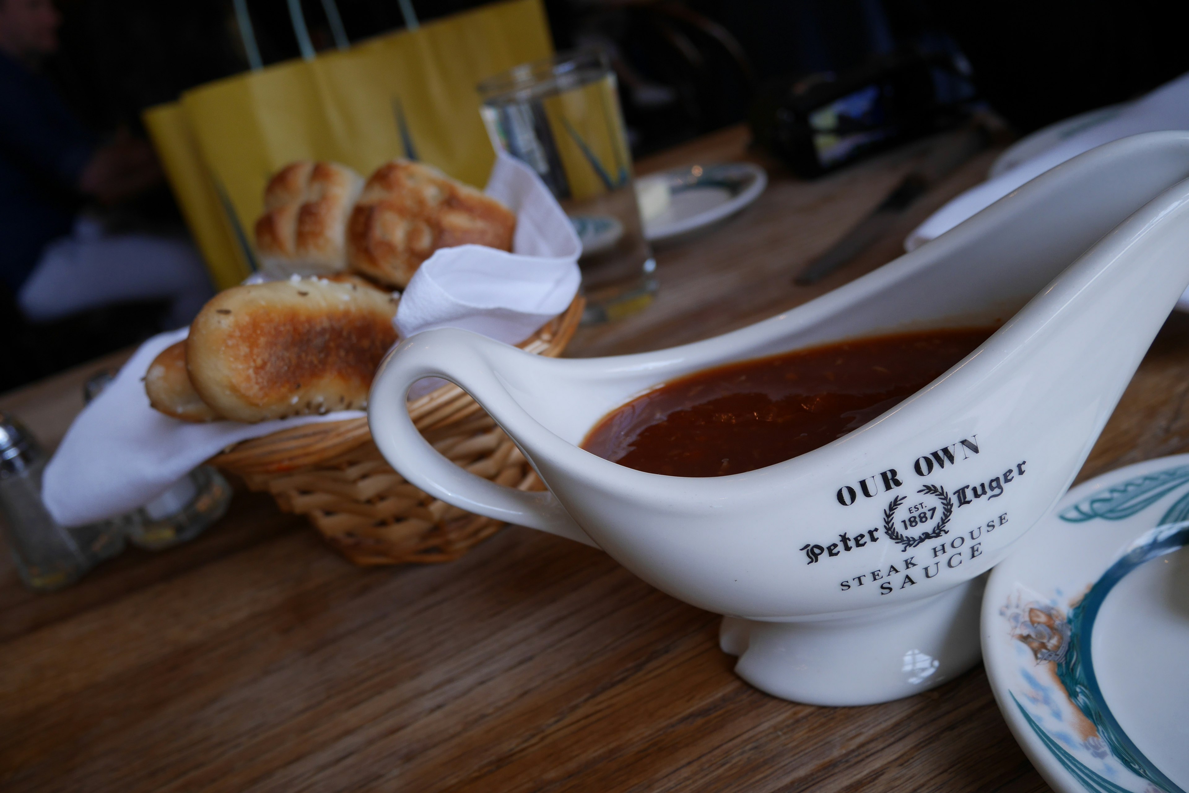 Gravy sauce in a white boat with a basket of bread rolls on a restaurant table