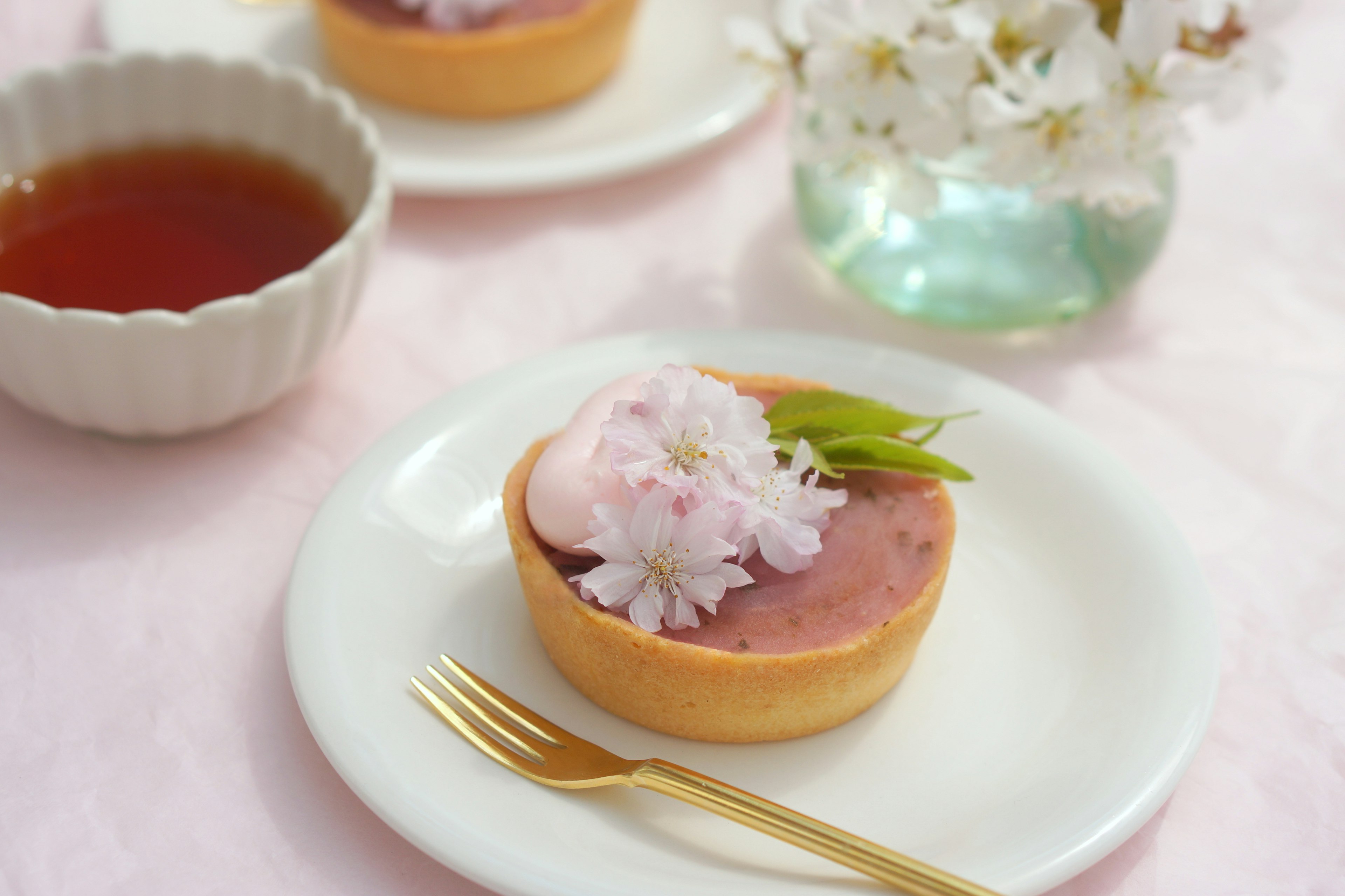 Japanese tart topped with cherry blossoms and a cup of green tea on a table