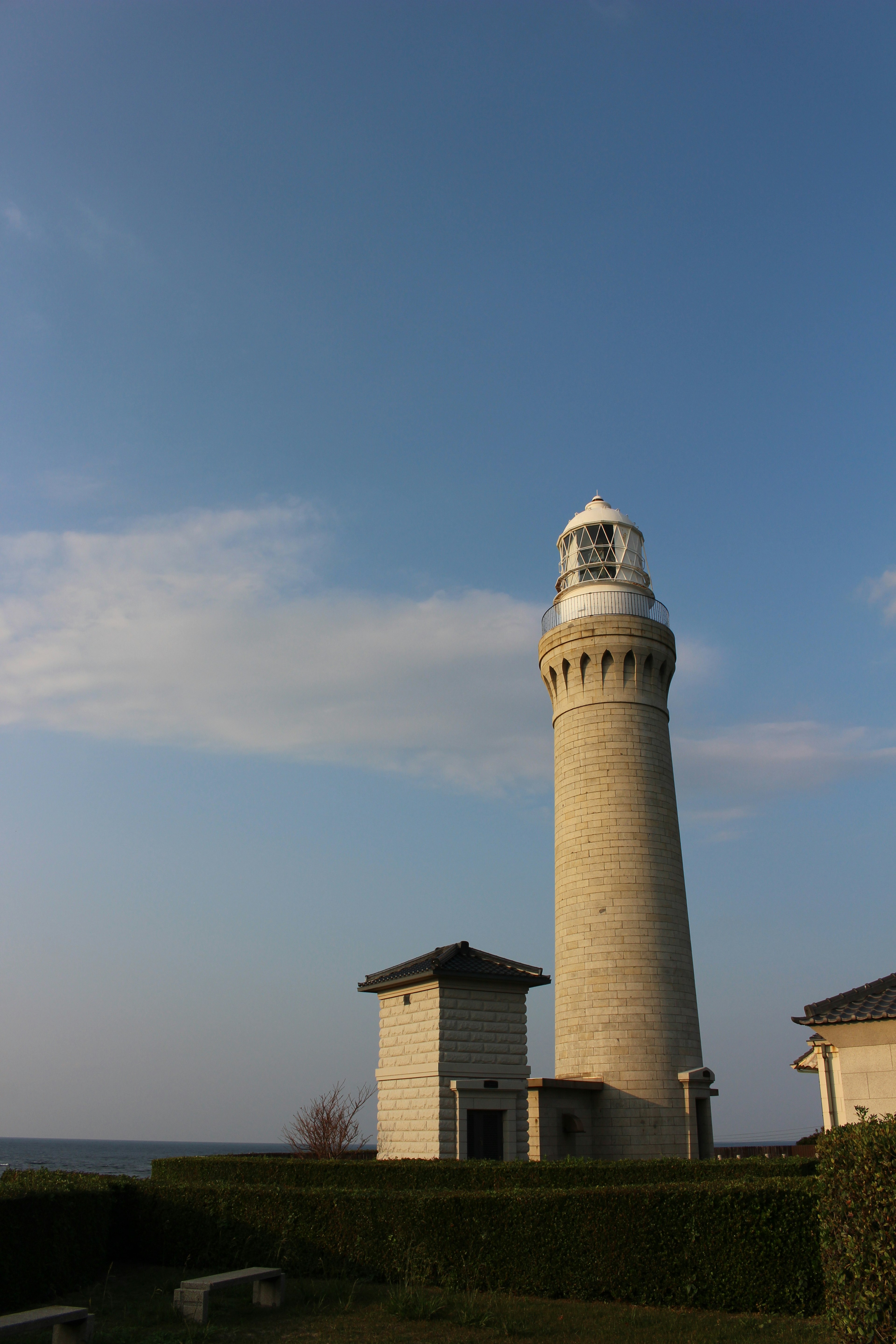 Lighthouse standing under a blue sky with surrounding buildings and greenery