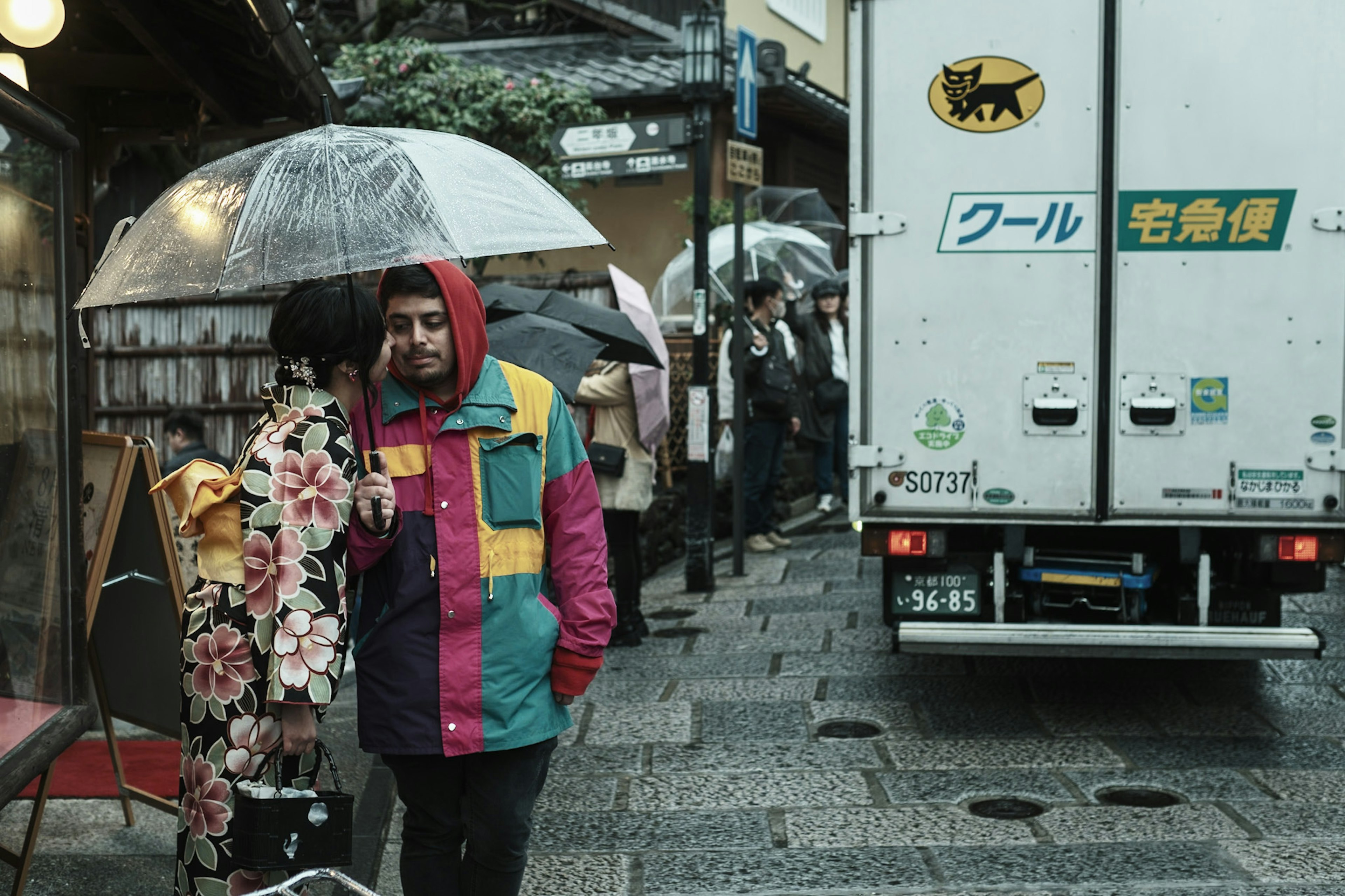 Two people in colorful clothing walking in the rain with umbrellas in a city street