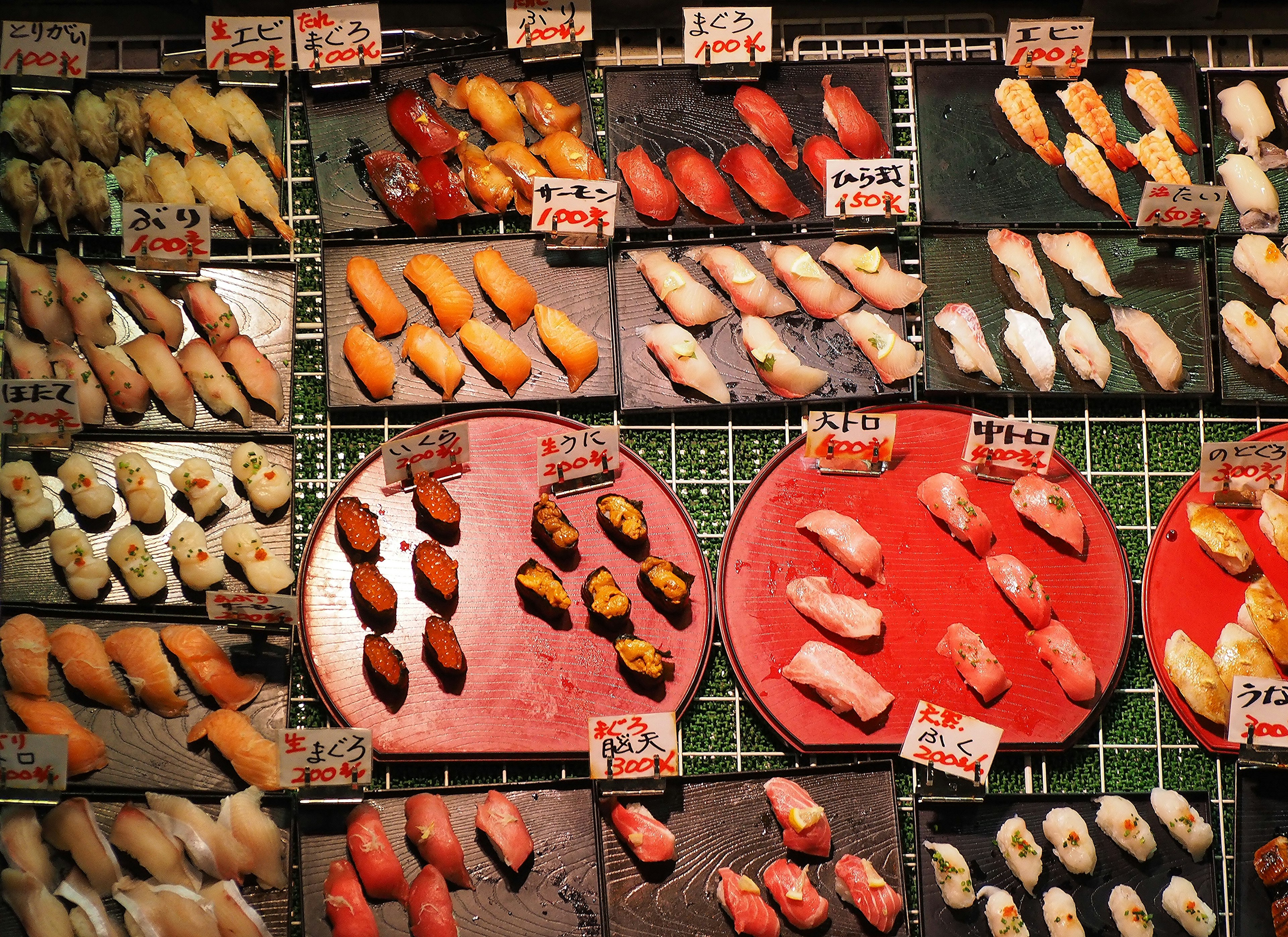 Colorful sushi display with various types arranged on plates and labels visible