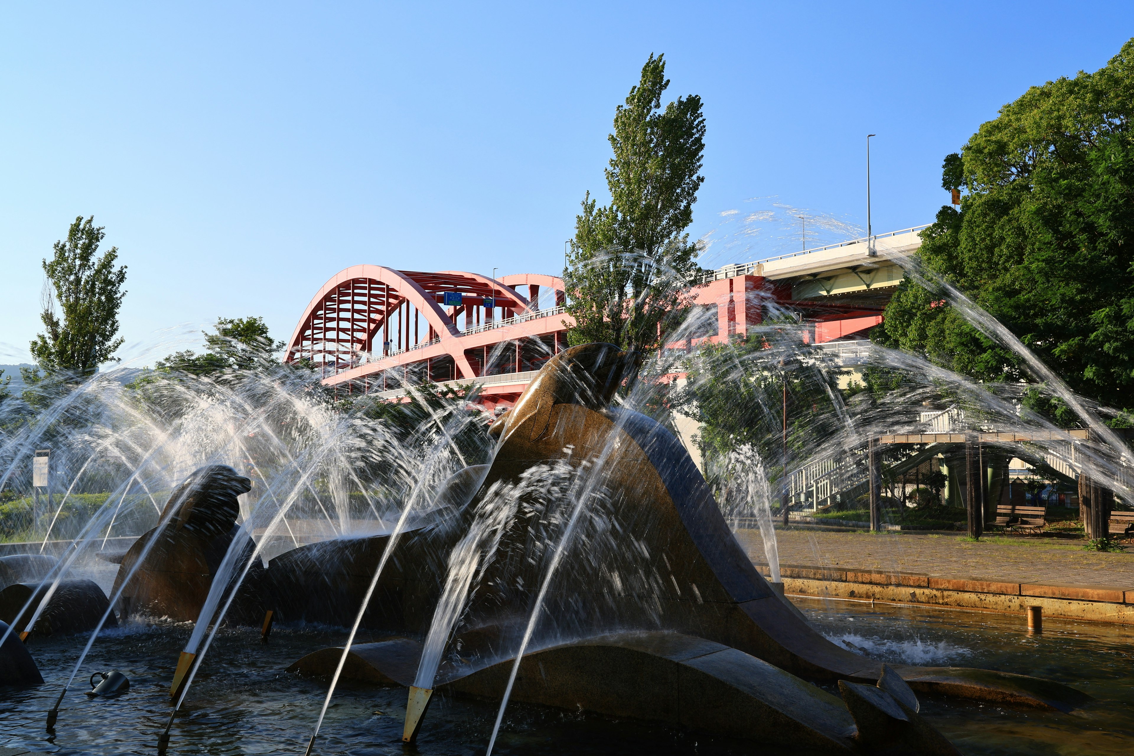 Fuente de parque con chorros de agua y un puente rojo al fondo