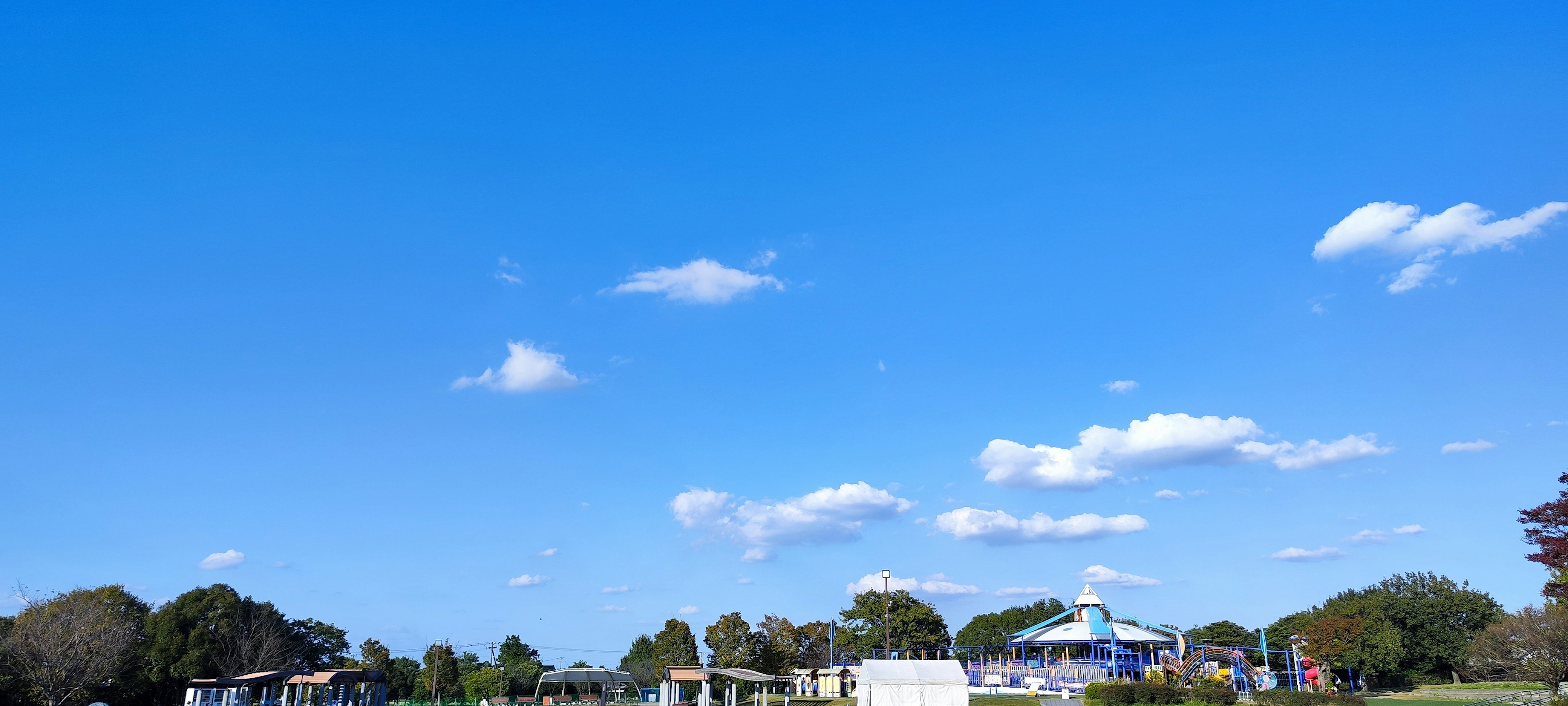 A landscape with blue sky and white clouds featuring green trees and buildings