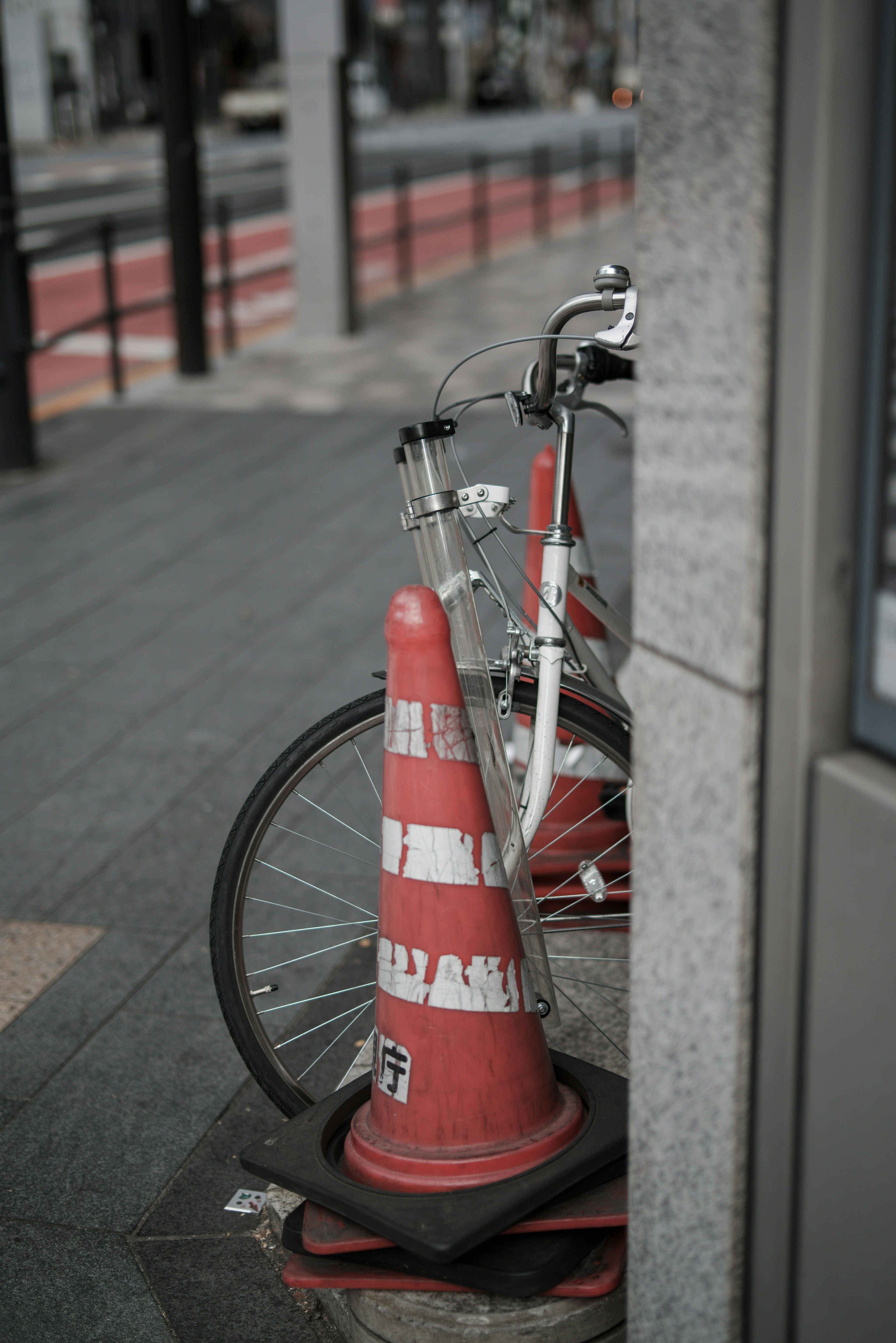 A white bicycle leaning against a red traffic cone on a city sidewalk