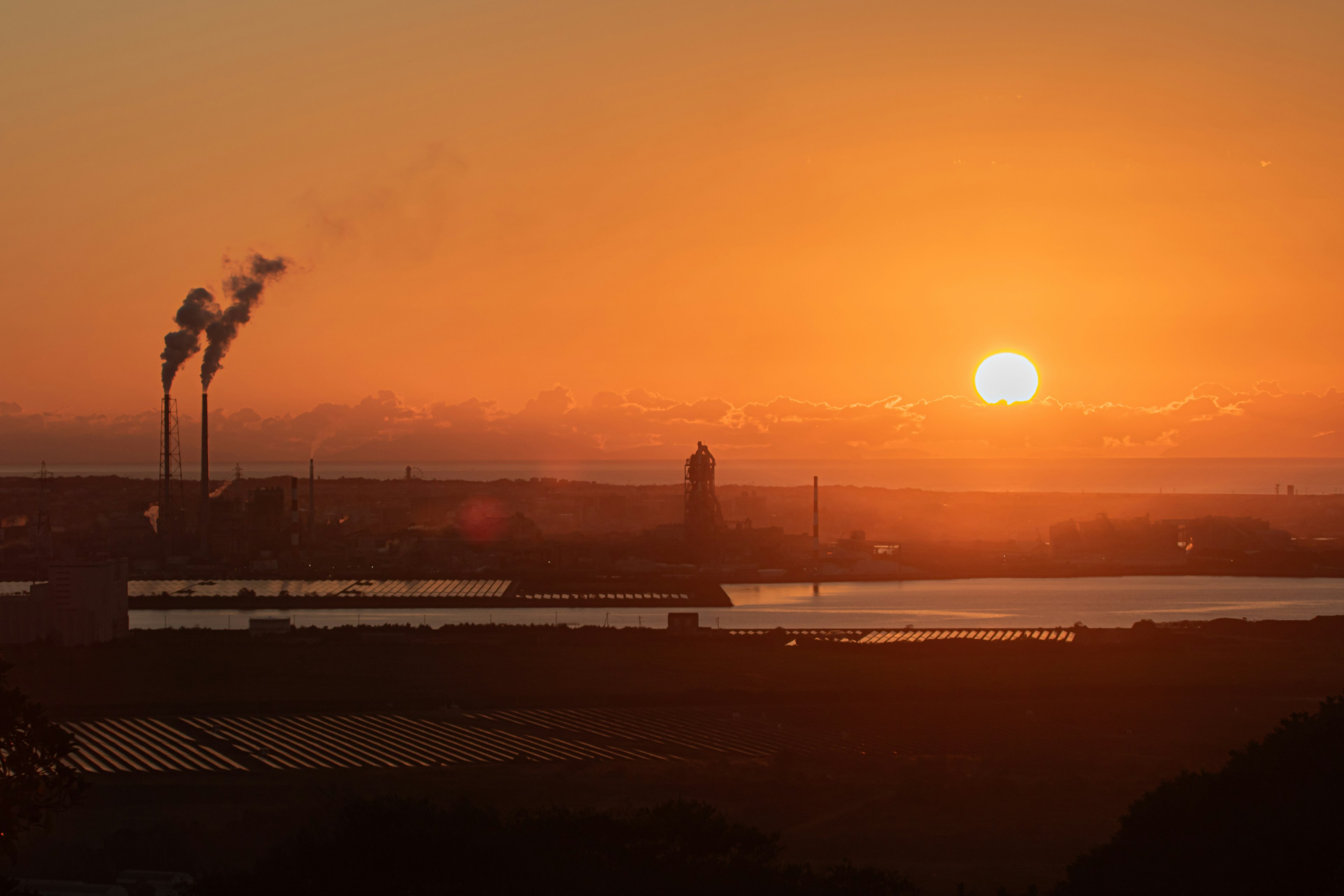 Paisaje industrial al atardecer con chimeneas y cielo naranja reflejado en el agua