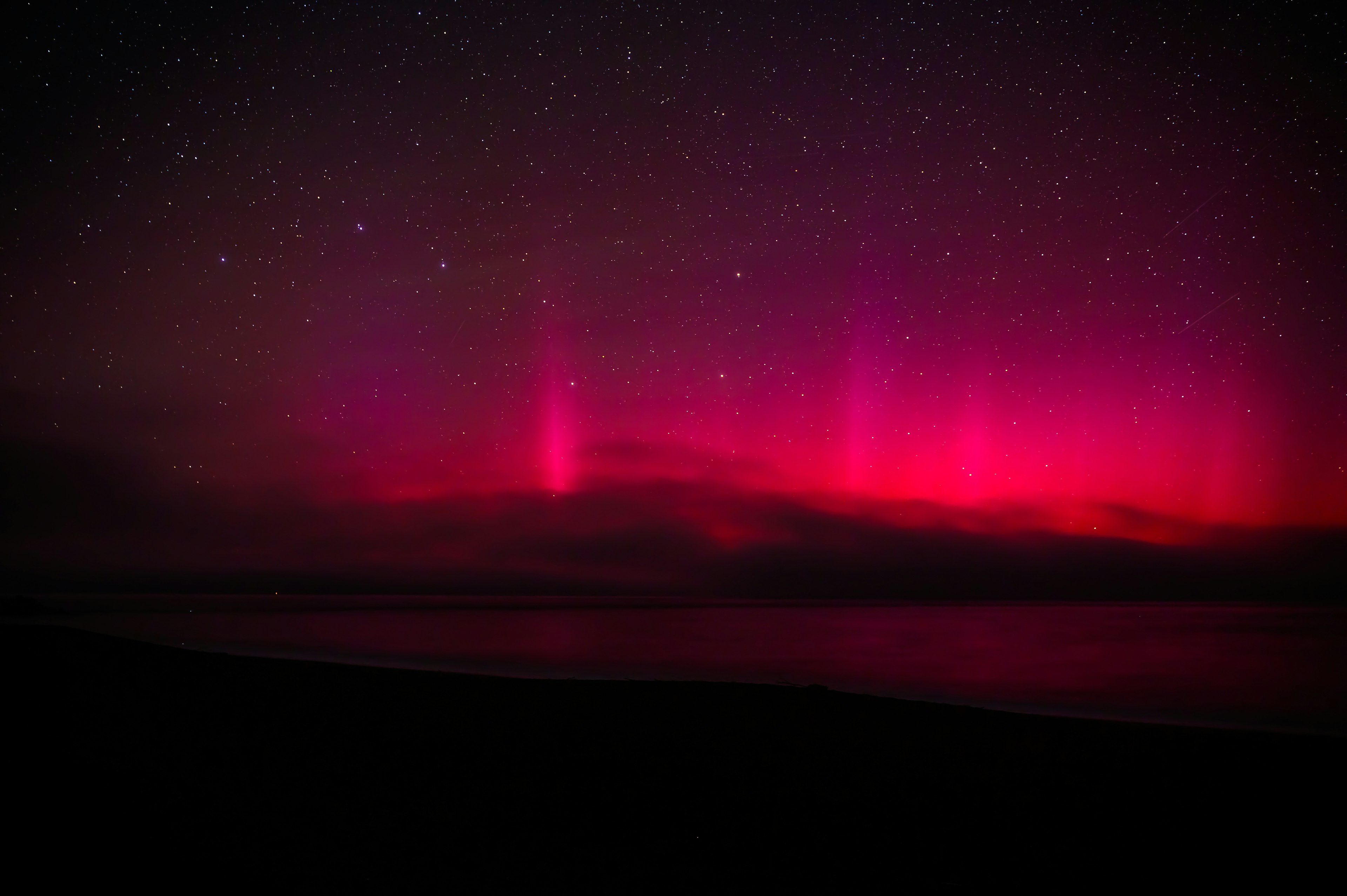 Aurora rosa vibrante sobre un océano oscuro bajo un cielo estrellado