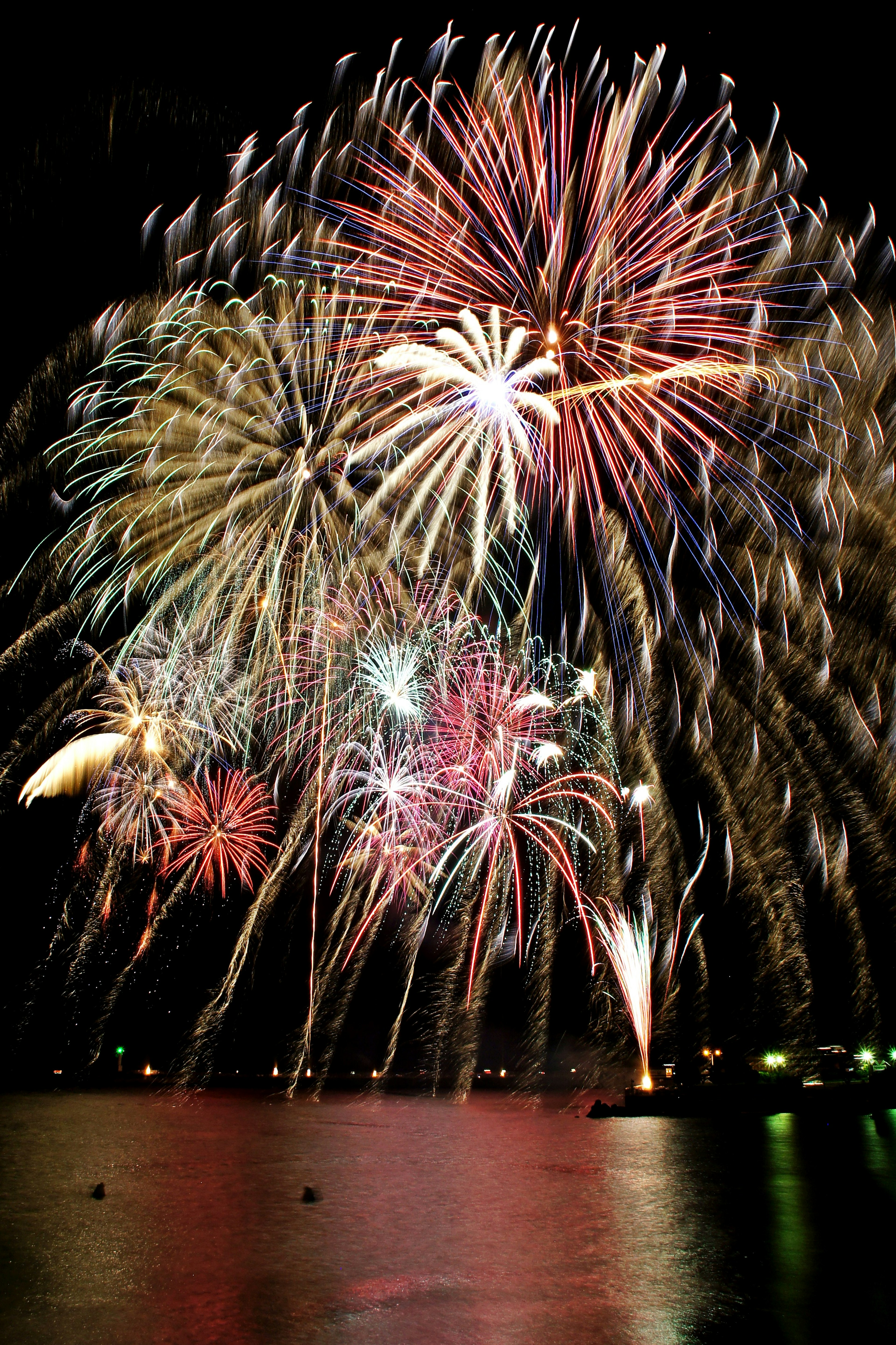 Des feux d'artifice colorés explosant dans le ciel nocturne se reflétant sur l'eau