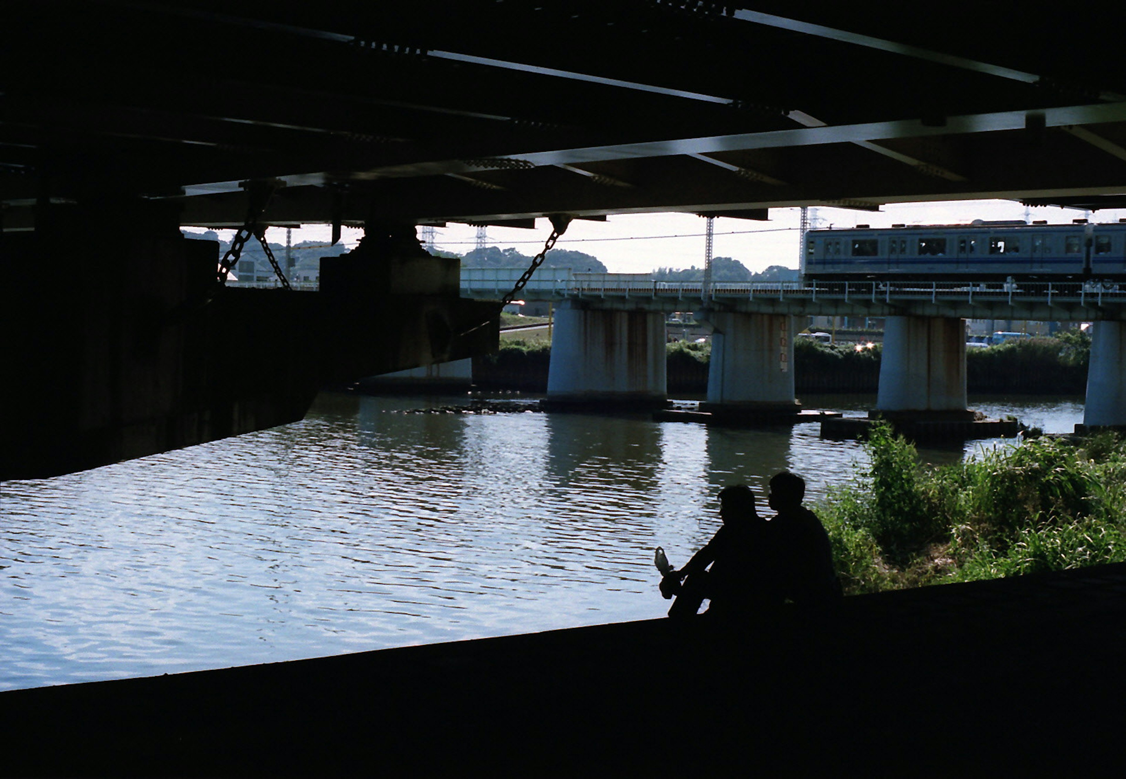 People sitting under a bridge with a calm water surface