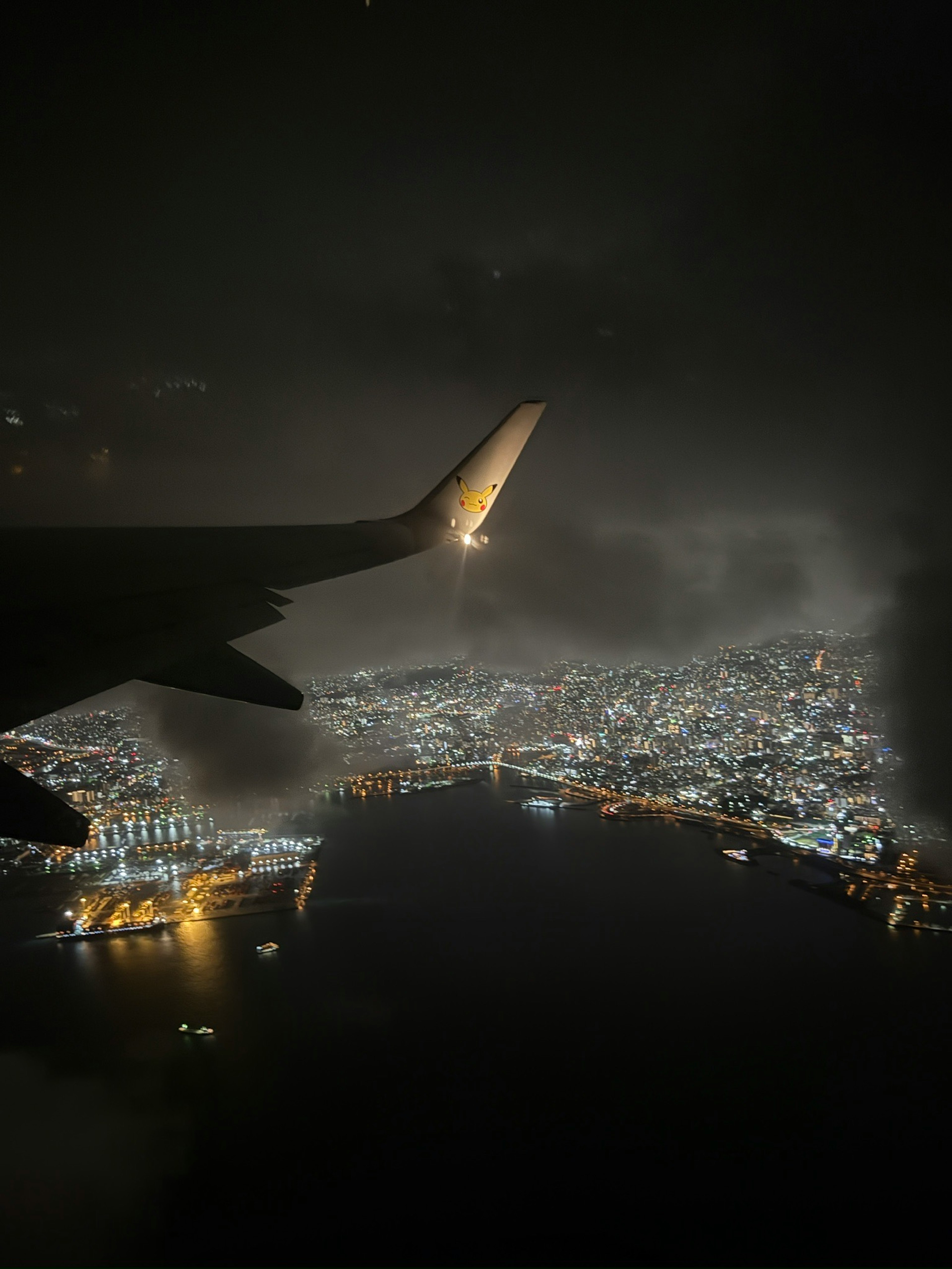 夜の都市景観を飛行機の窓から見下ろす光景で、街の明かりが美しく輝いている