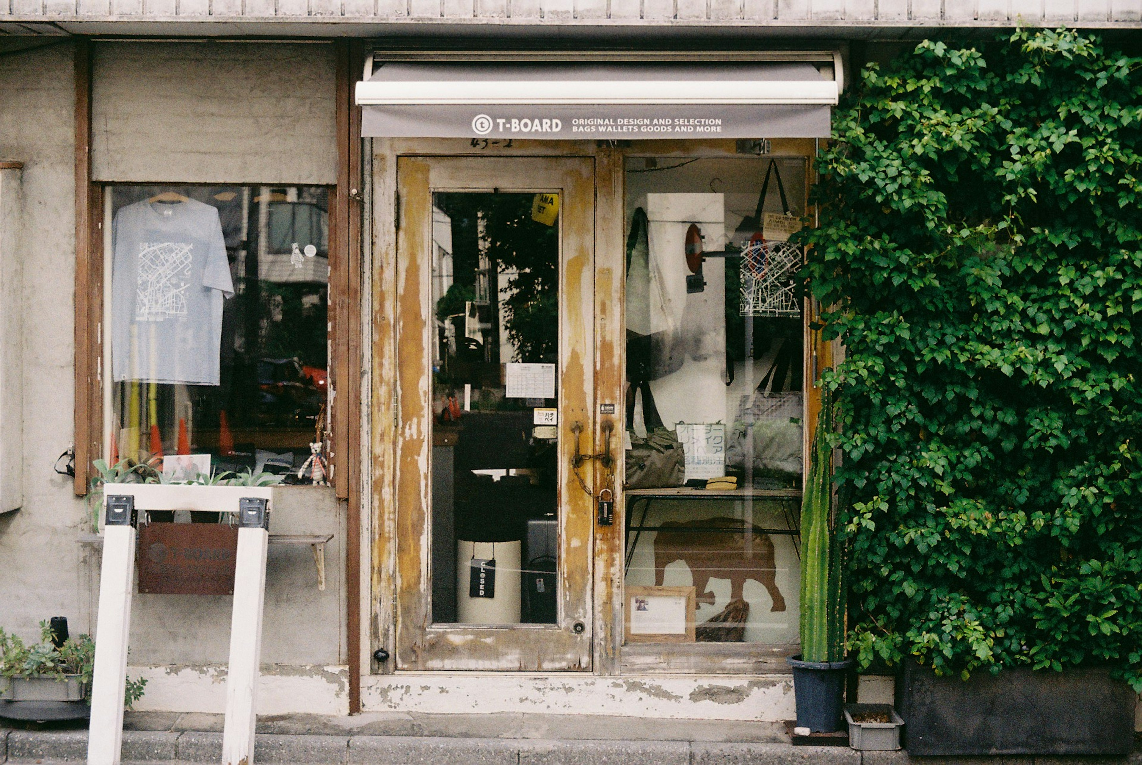 Entrada de una tienda antigua con puertas de madera rodeadas de vegetación exhibiendo ropa