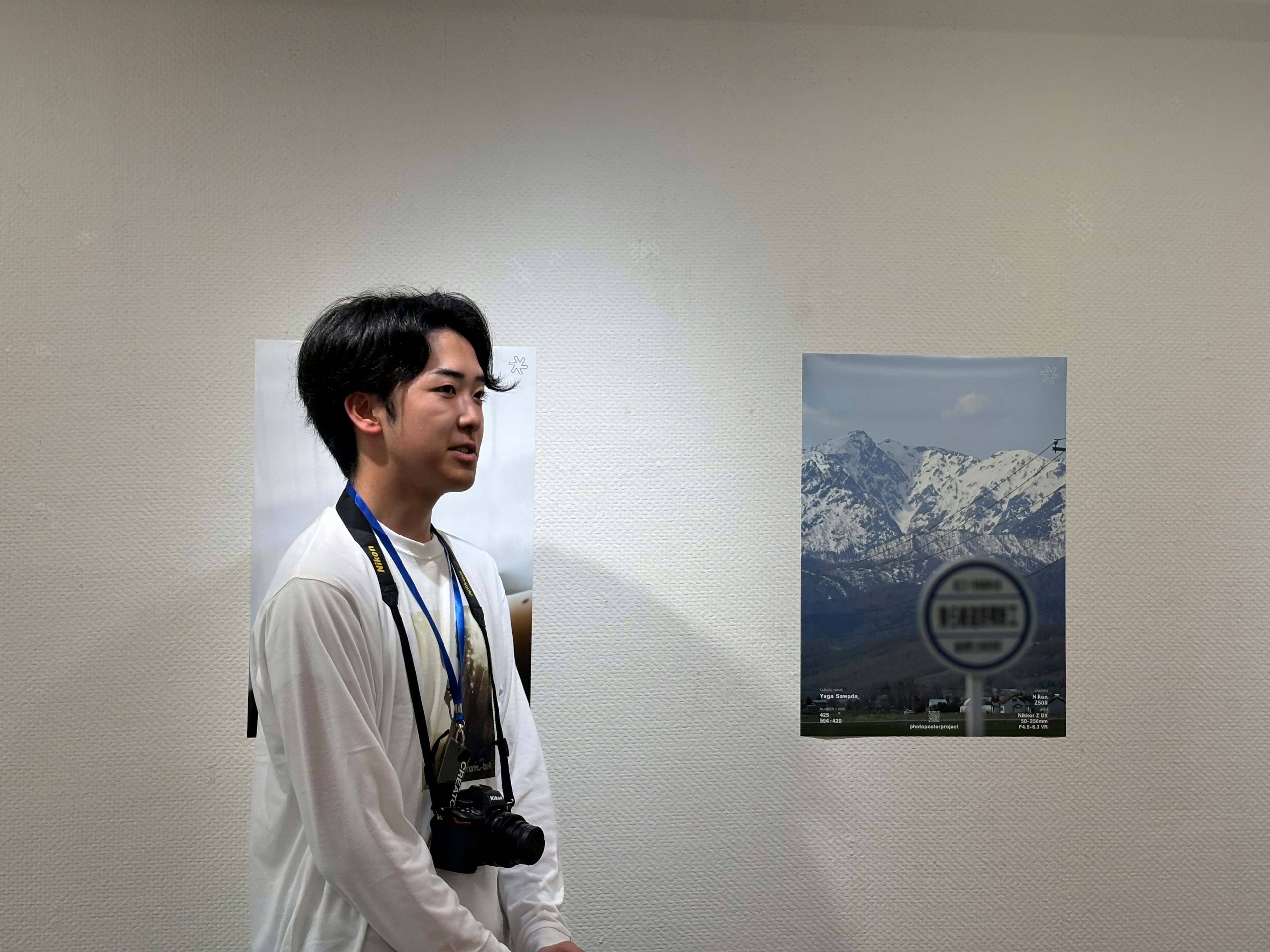 Junger Mann mit einer Kamera steht neben einem Bergposter