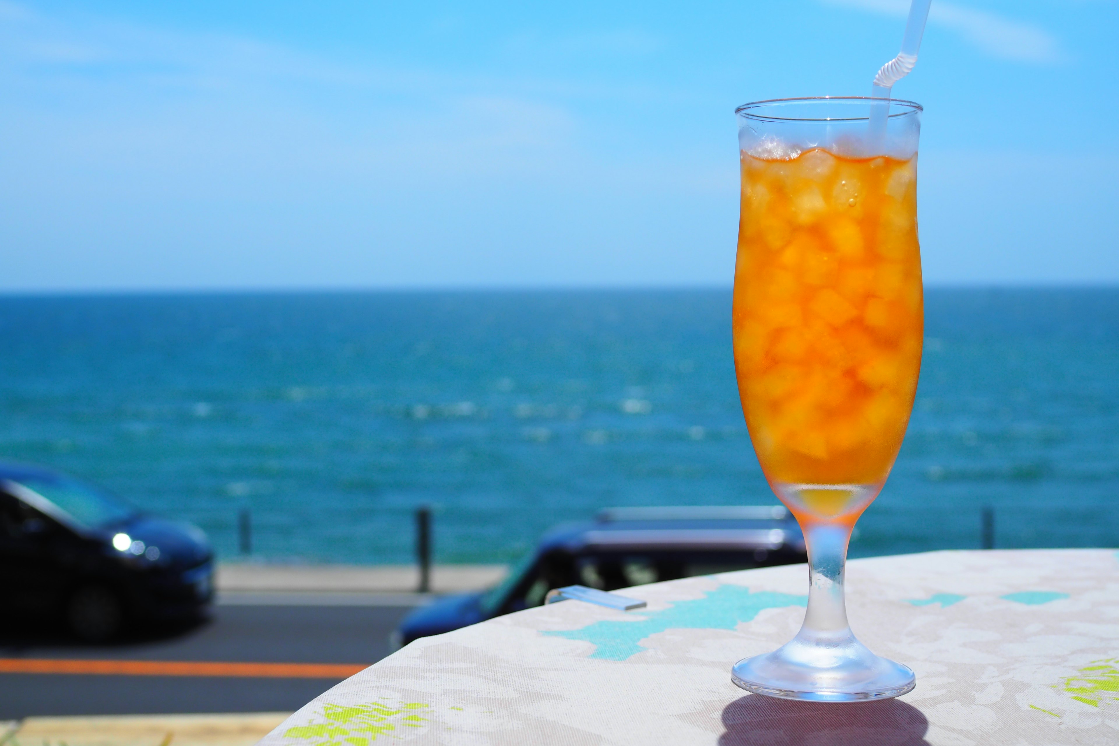 Ein Glas mit orangefarbenem Getränk und Eis vor einem blauen Meer