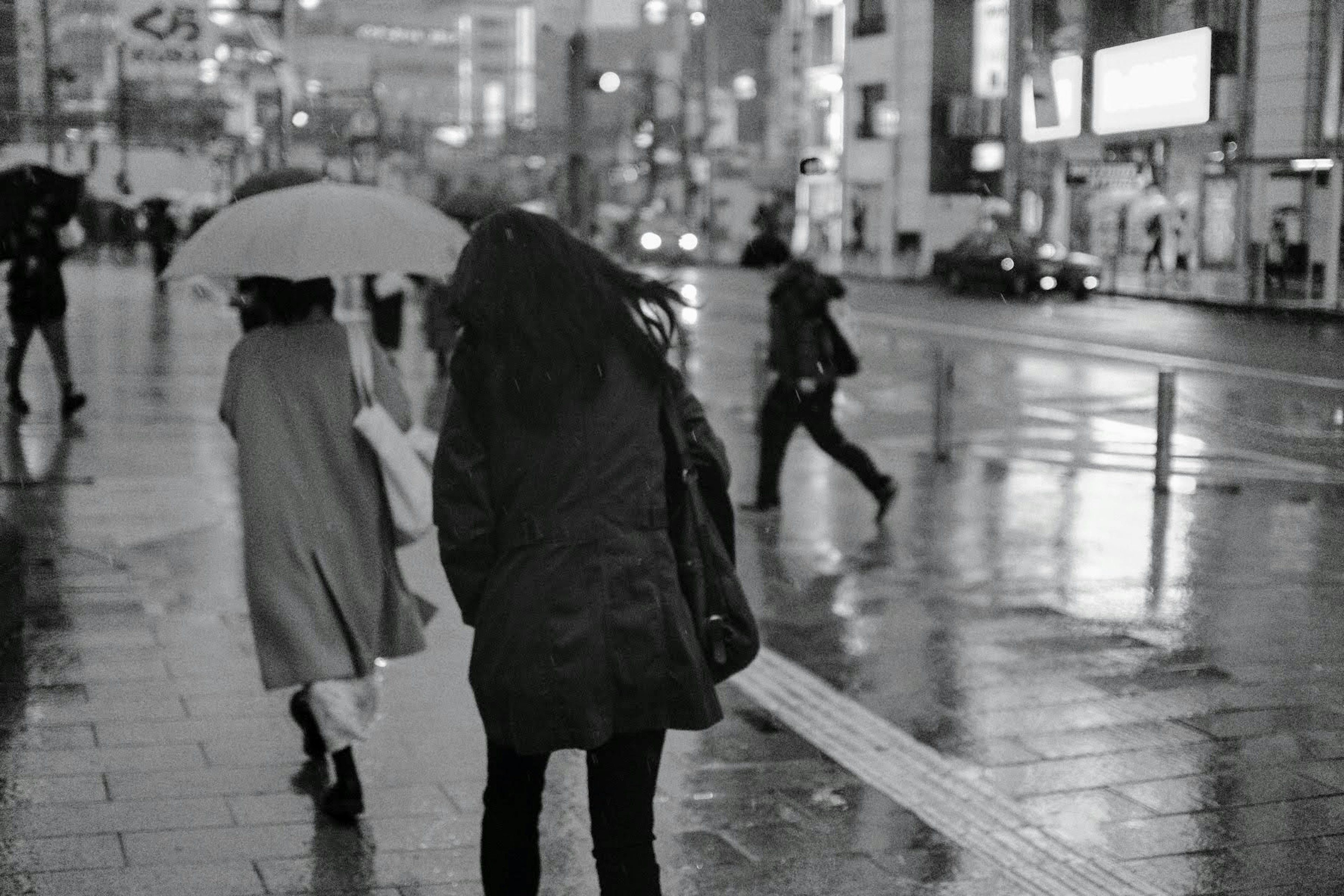 雨の中を歩く人々のモノクロ写真傘を持つ女性と後ろ姿の女性