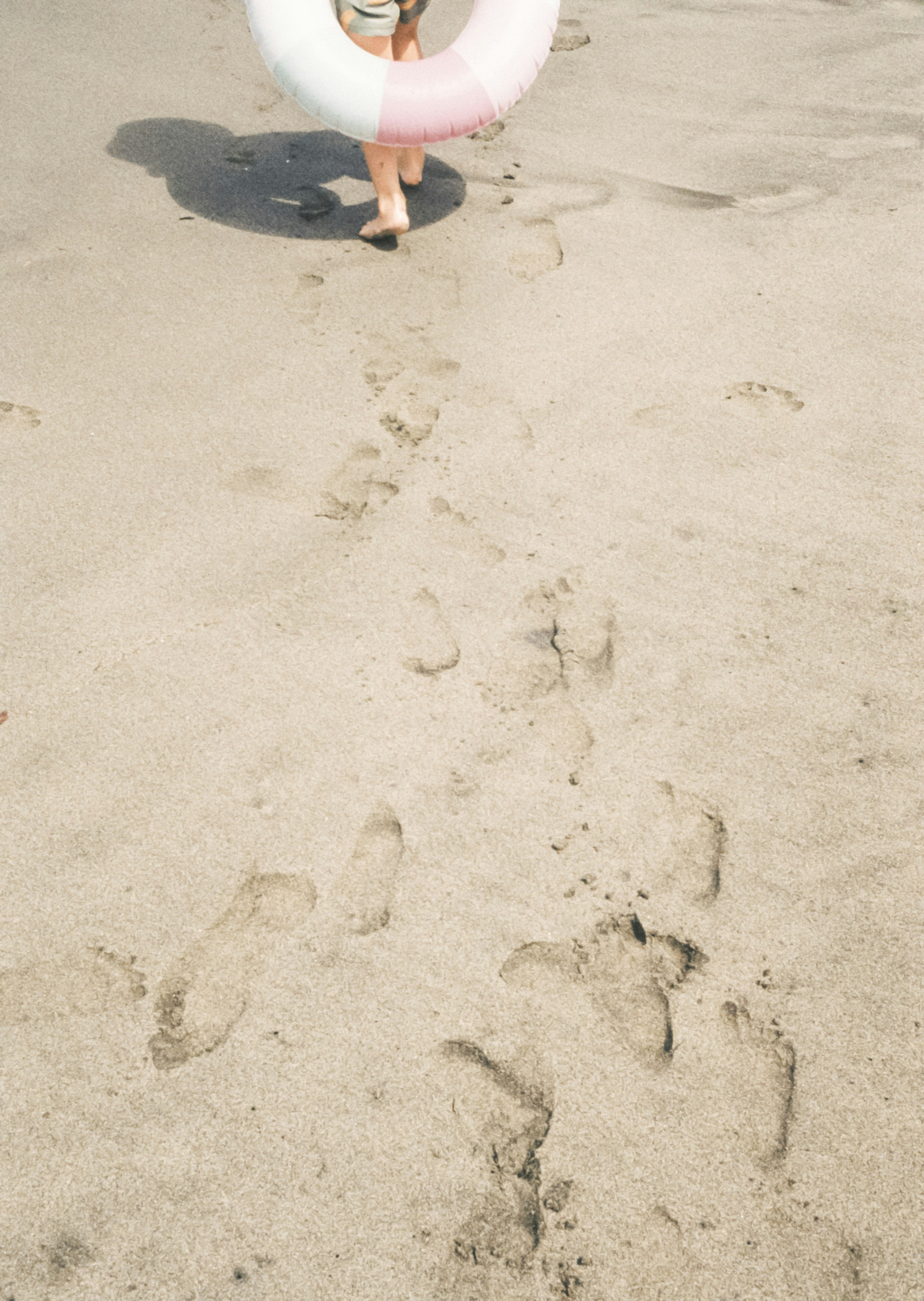 砂浜を歩く子供と浮き輪の跡