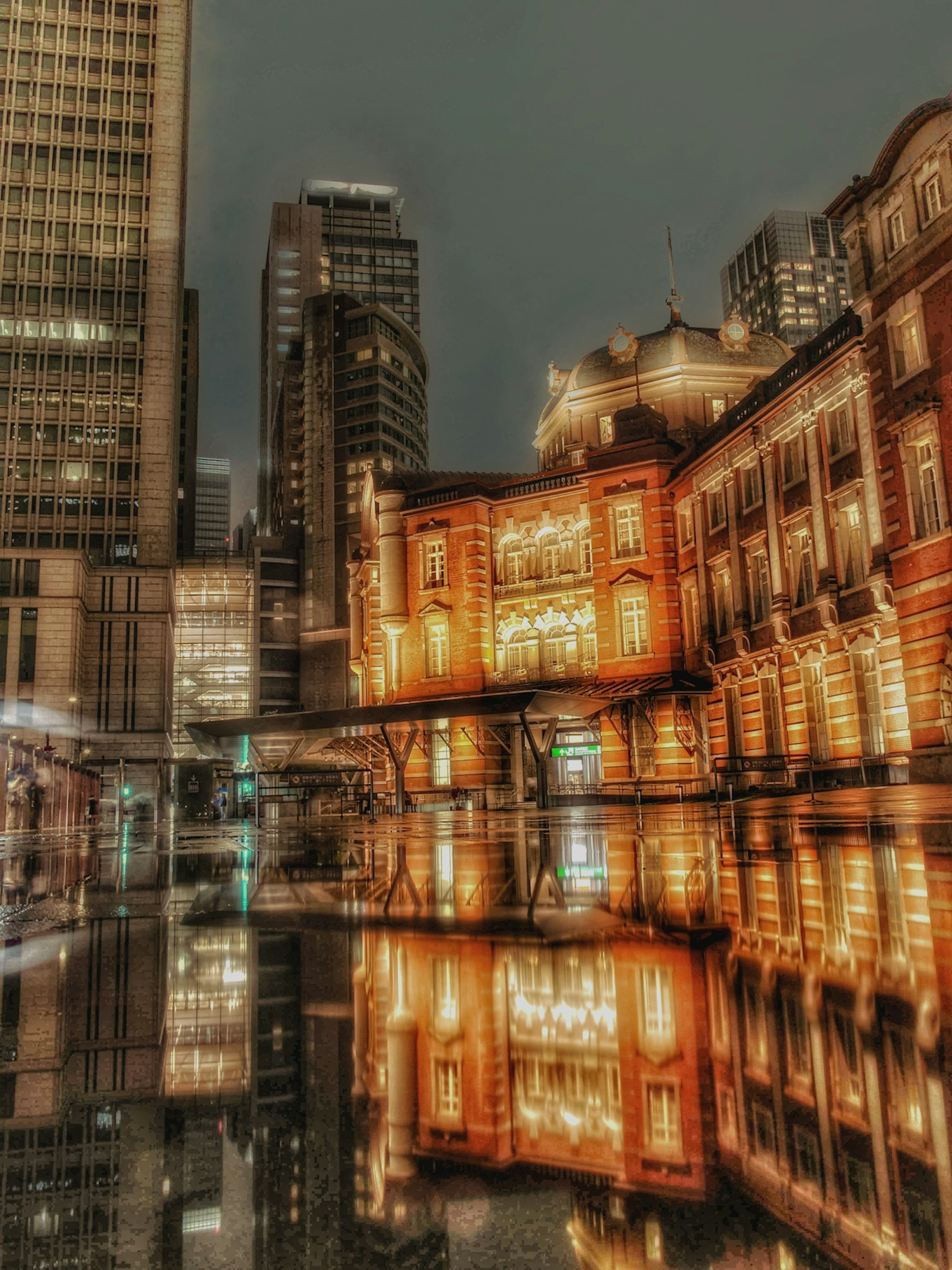 Gare de Tokyo illuminée la nuit avec des reflets dans l'eau et des gratte-ciels environnants