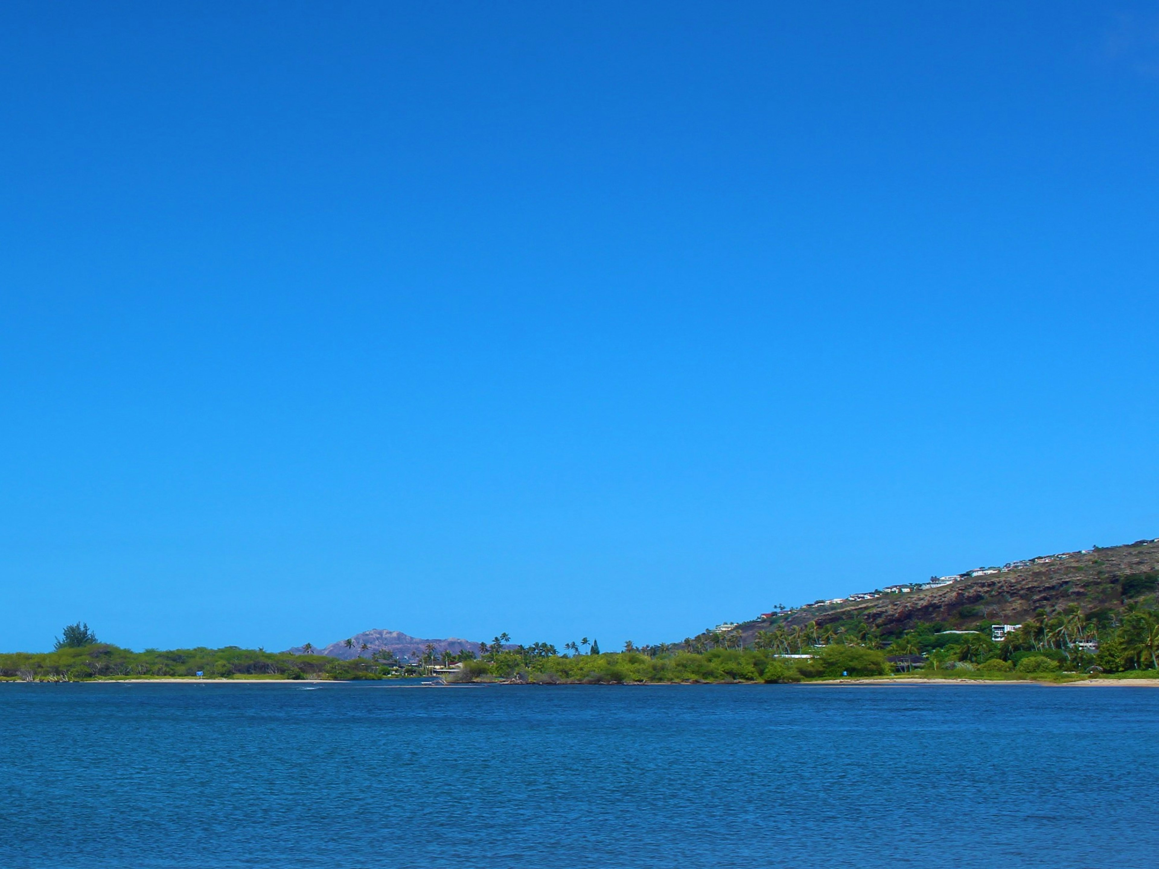 Landscape featuring a clear blue sky and calm water surface with green hills in the distance