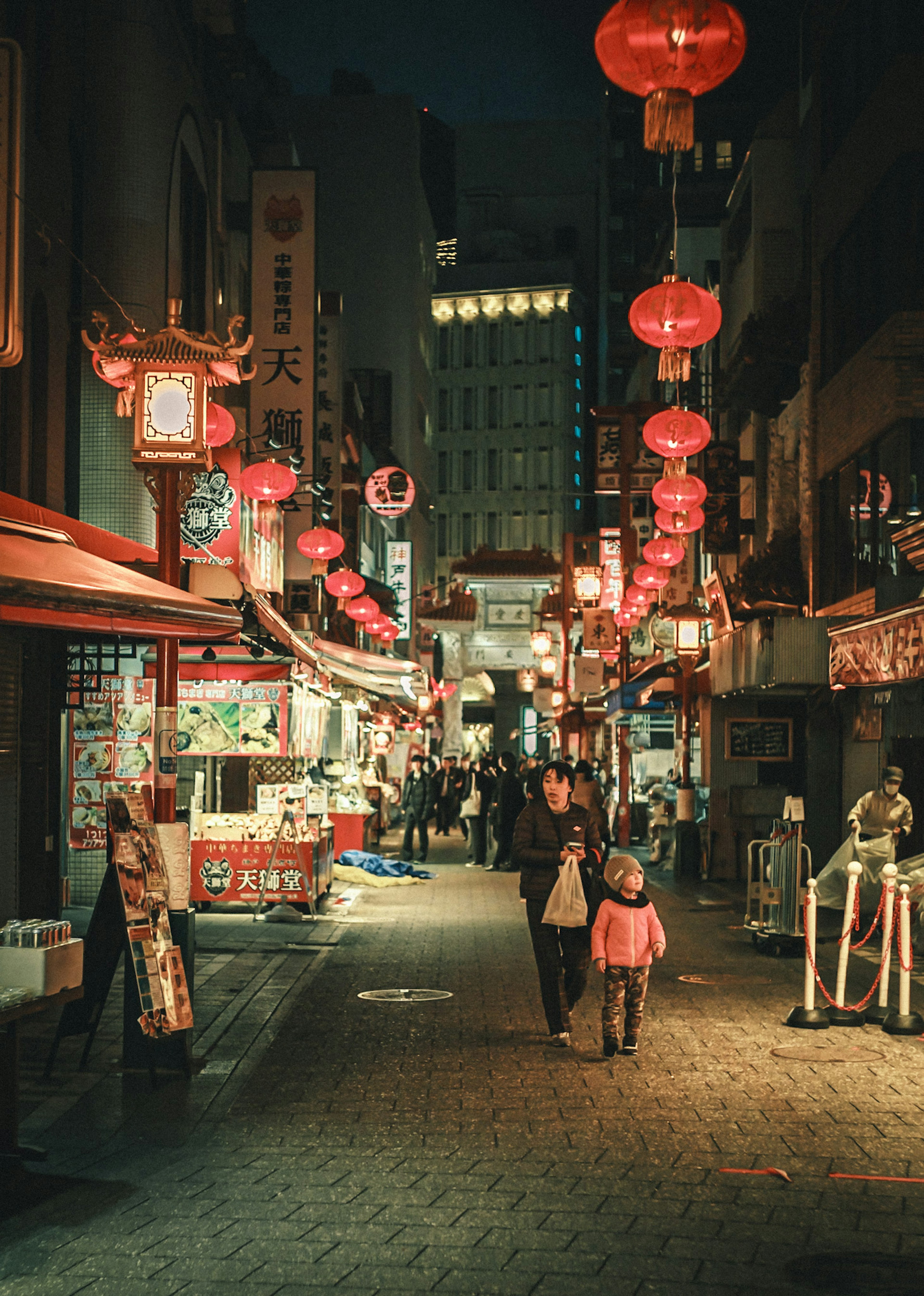 夜の街並みに吊るされた赤いランタンと人々が歩く様子