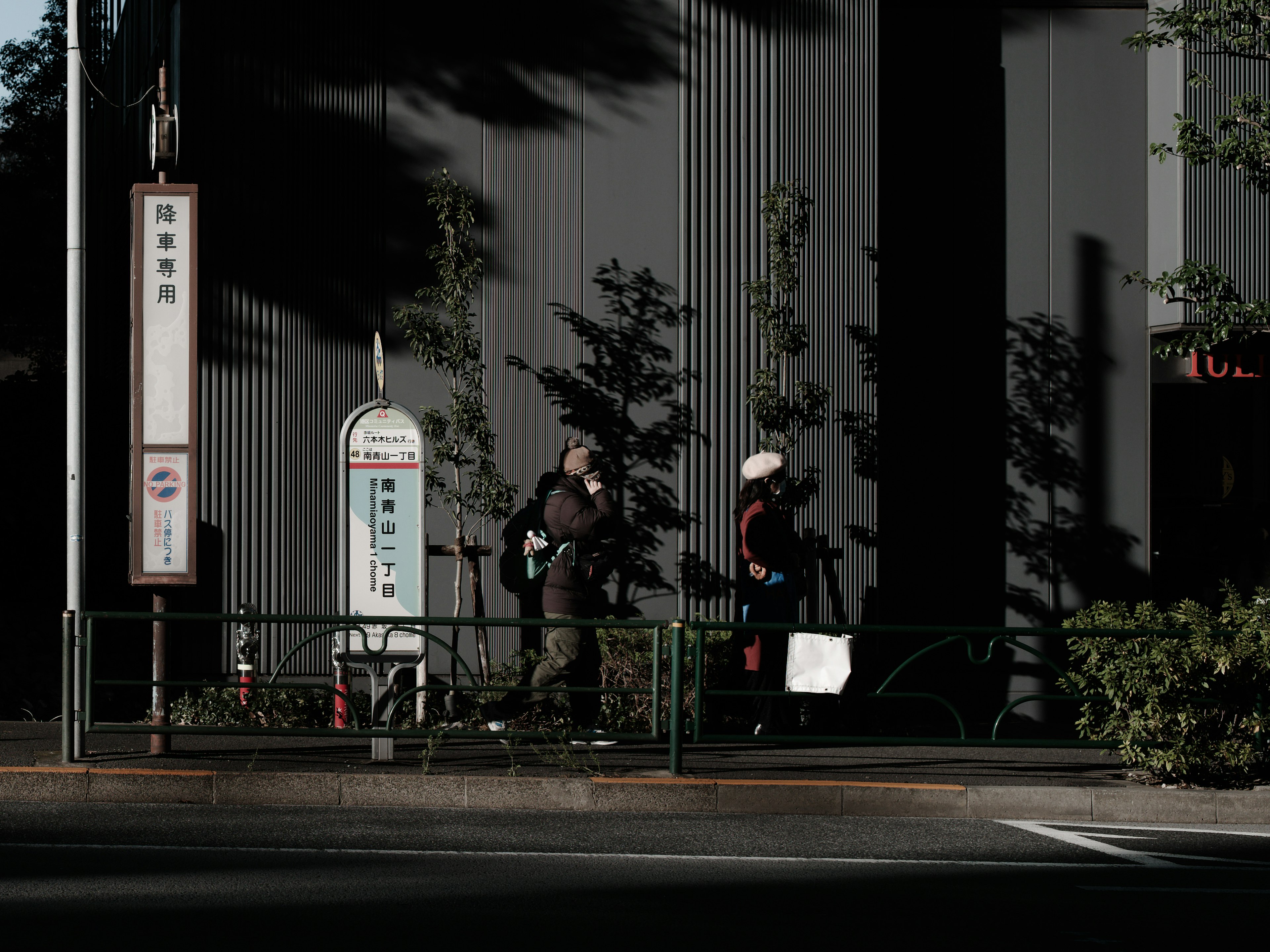 People waiting at a street bus stop with shadows and urban details