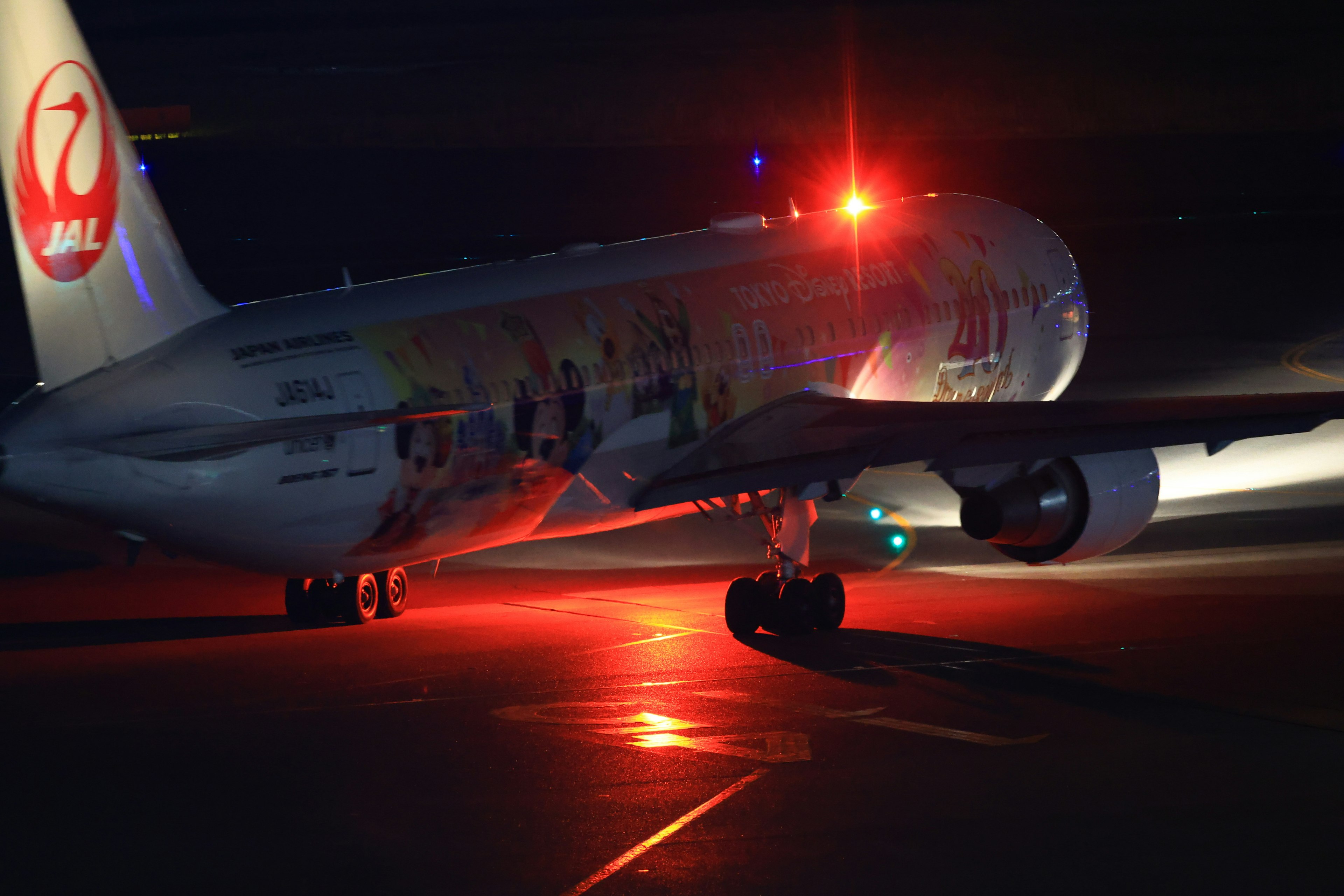 Avión rodando en la pista de noche con luces rojas intermitentes y diseño colorido