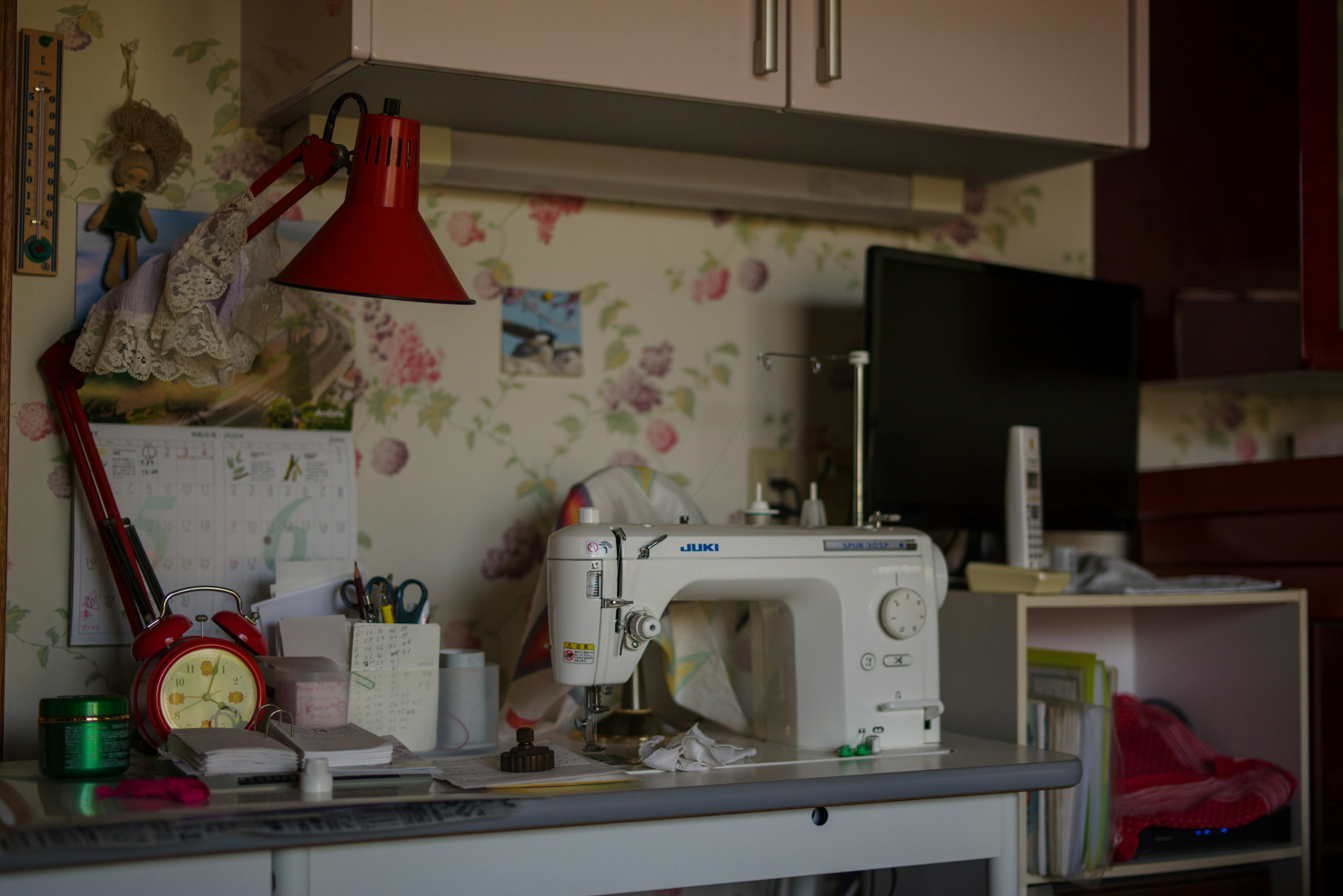 Bright red lamp on a sewing workspace with floral wallpaper in the background