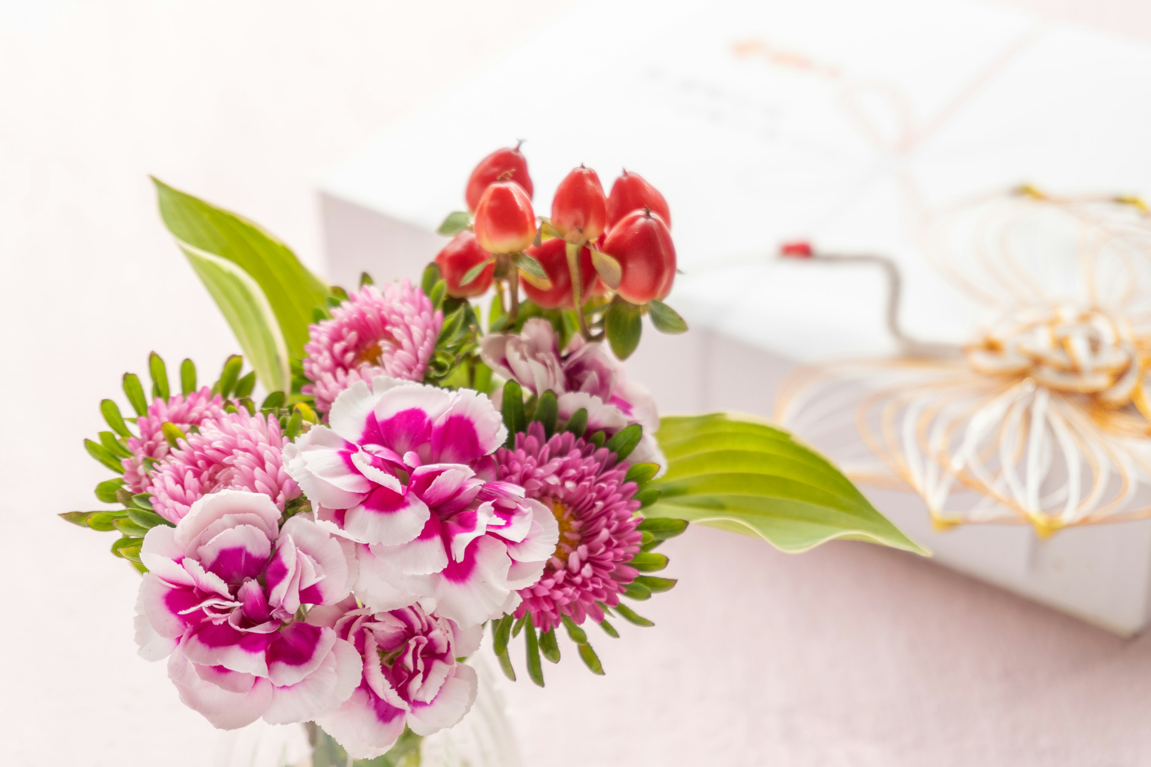 Un bel arrangement de fleurs roses et de feuilles vertes sur une table à côté d'une boîte cadeau