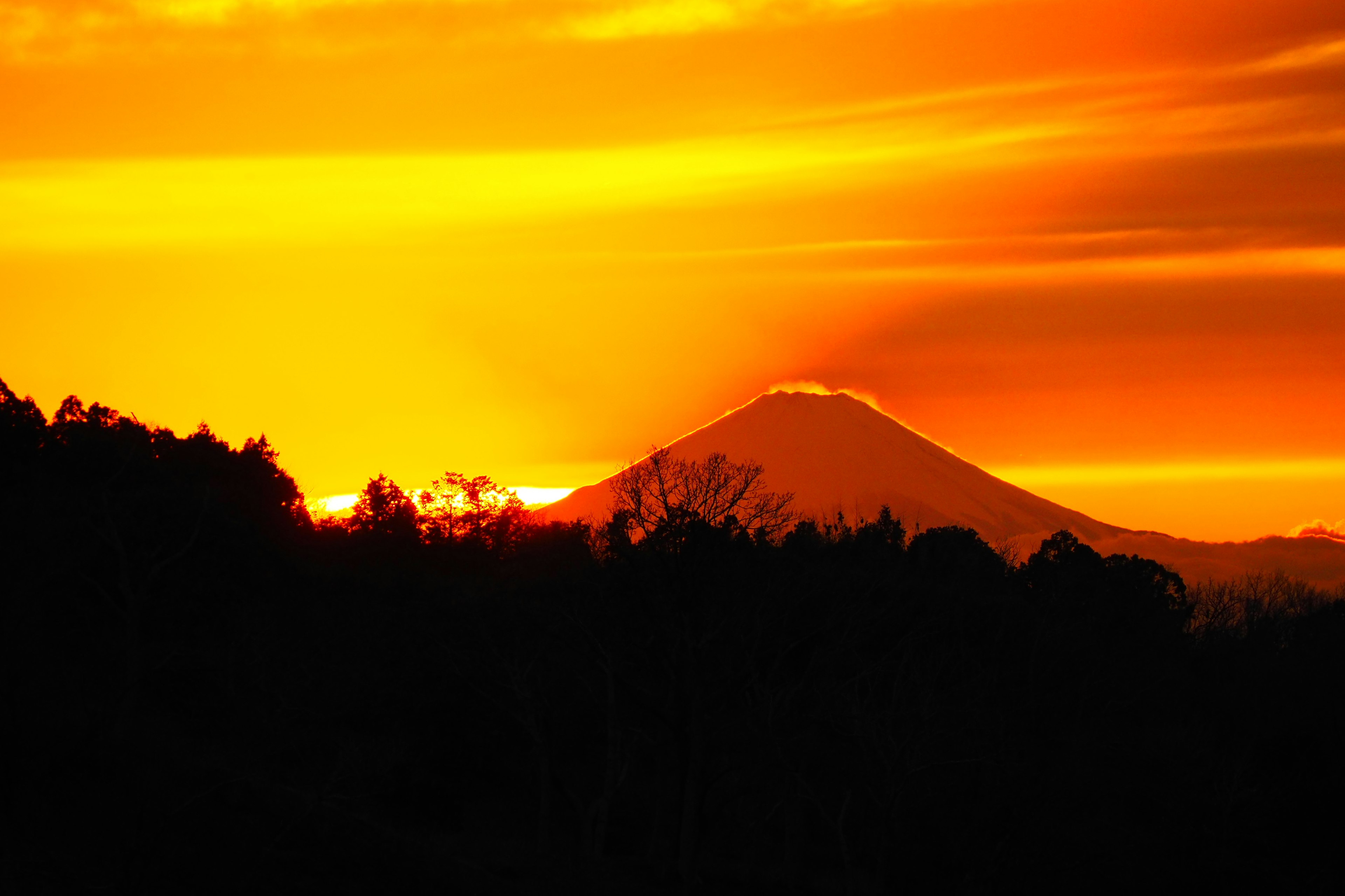 Silhouette gunung melawan matahari terbenam yang cerah