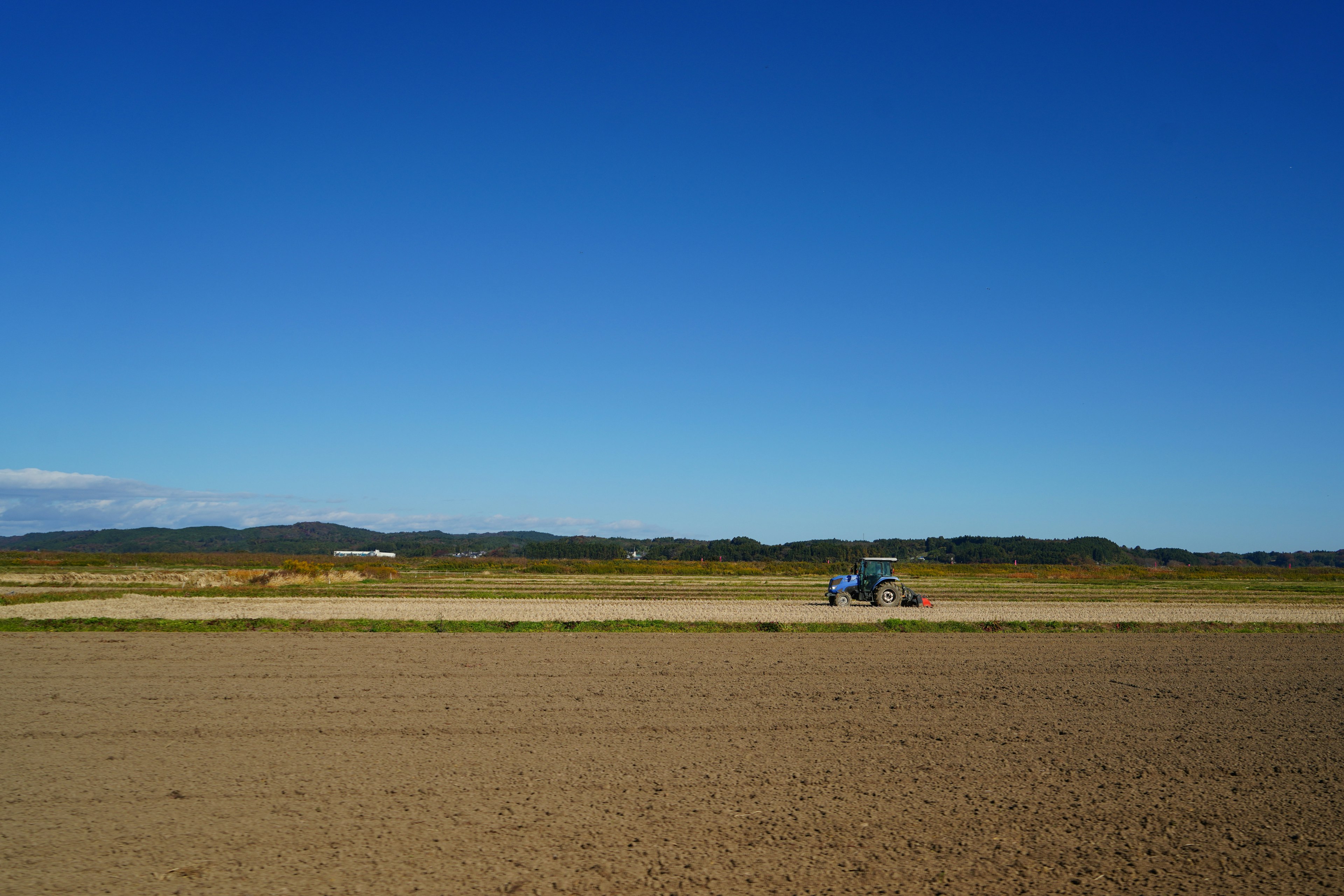 Un trattore che lavora su un vasto terreno agricolo sotto un cielo blu chiaro