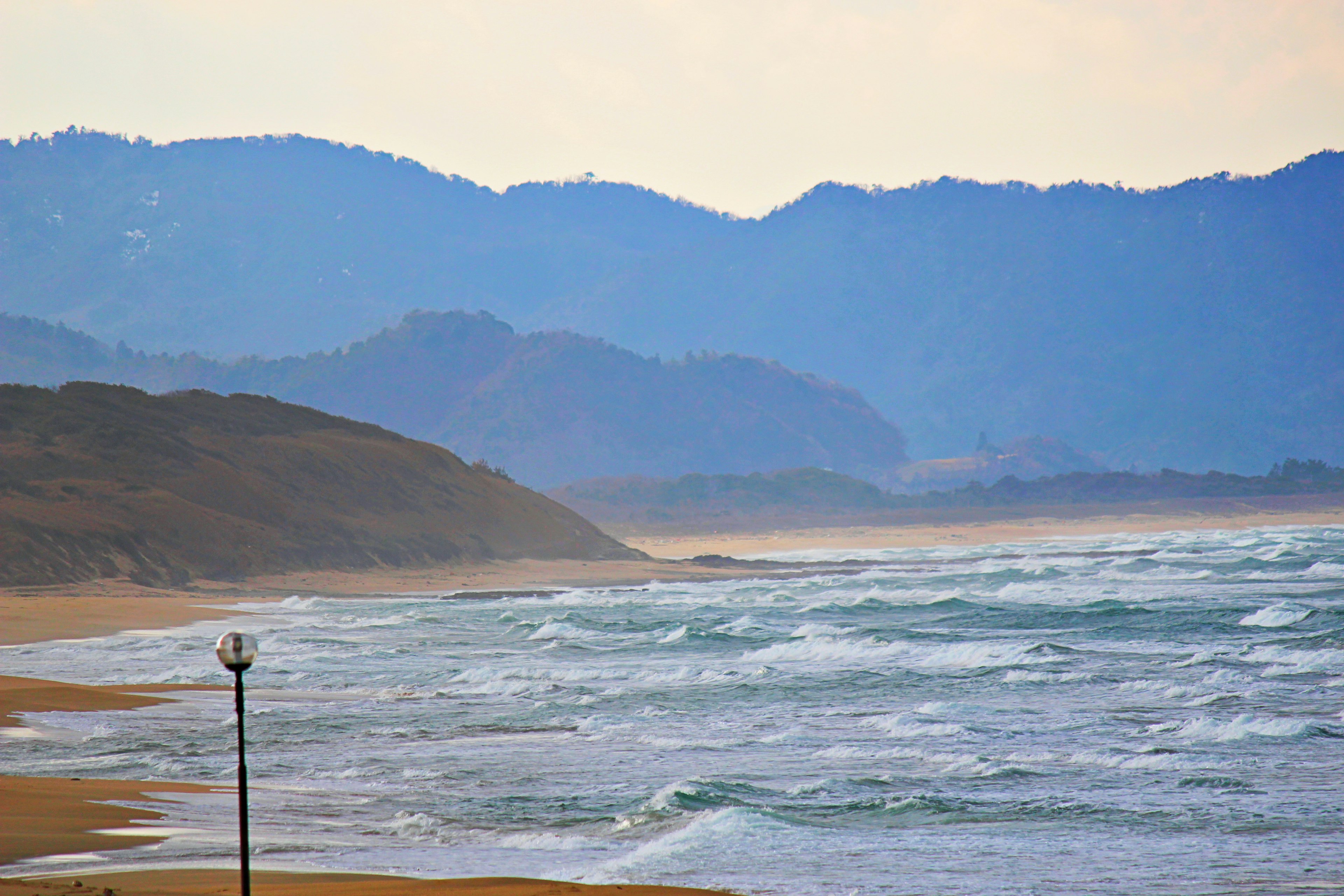 风景如画的海滩景观，背景是蓝色山脉和波涛汹涌的大海