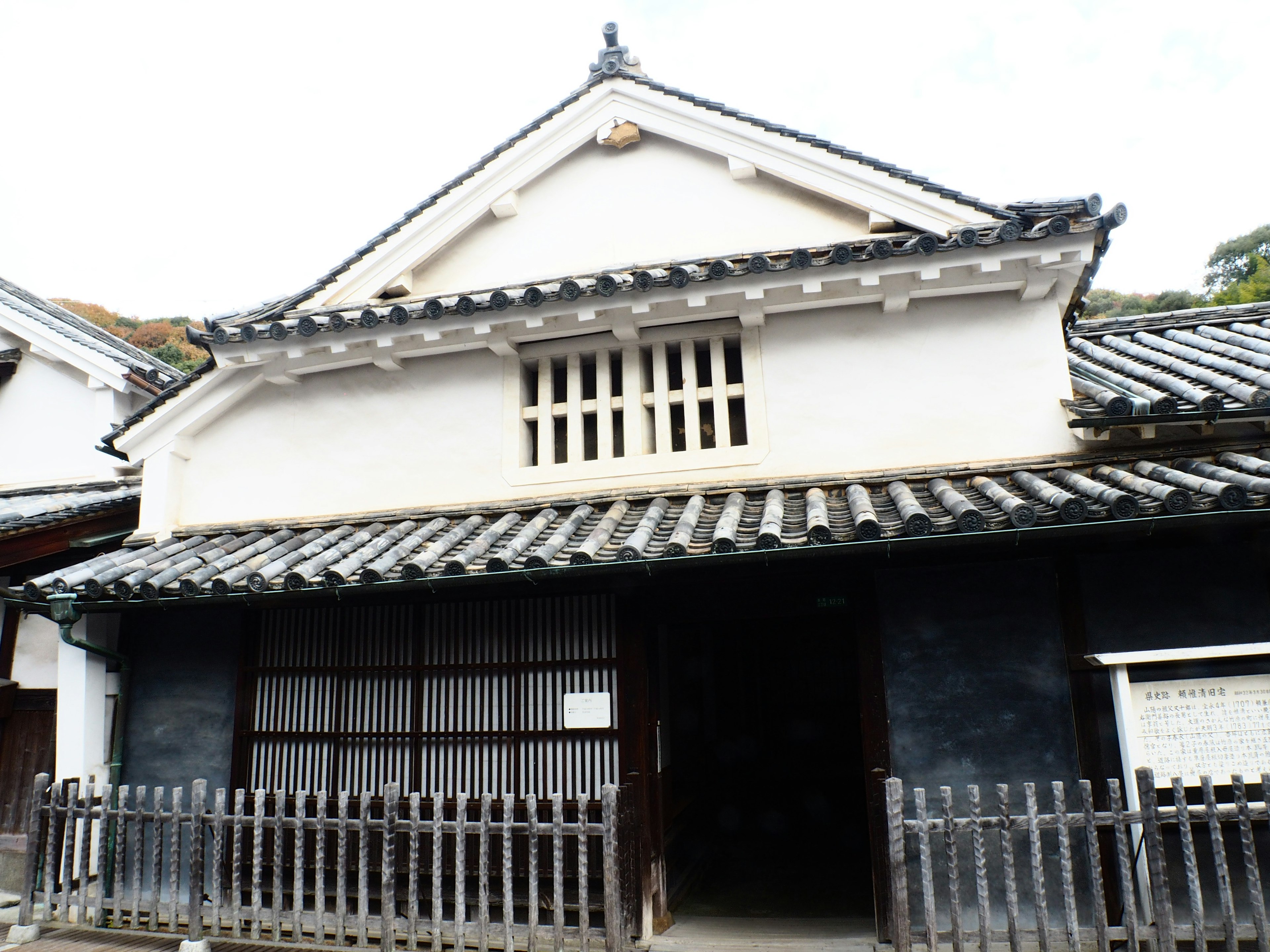 Traditionelles japanisches Gebäude mit weißer Fassade und Ziegeldach, umgeben von einem Holzzaun