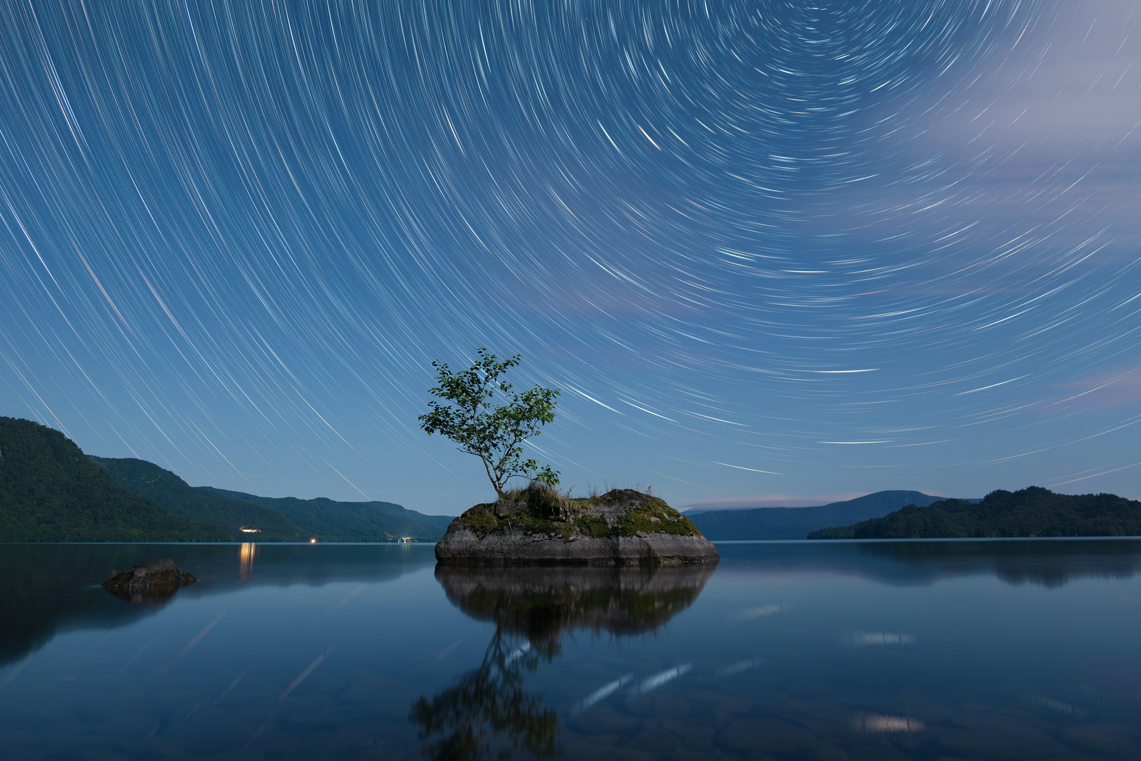 Una pequeña isla con un árbol bajo un cielo estrellado que muestra estelas de estrellas