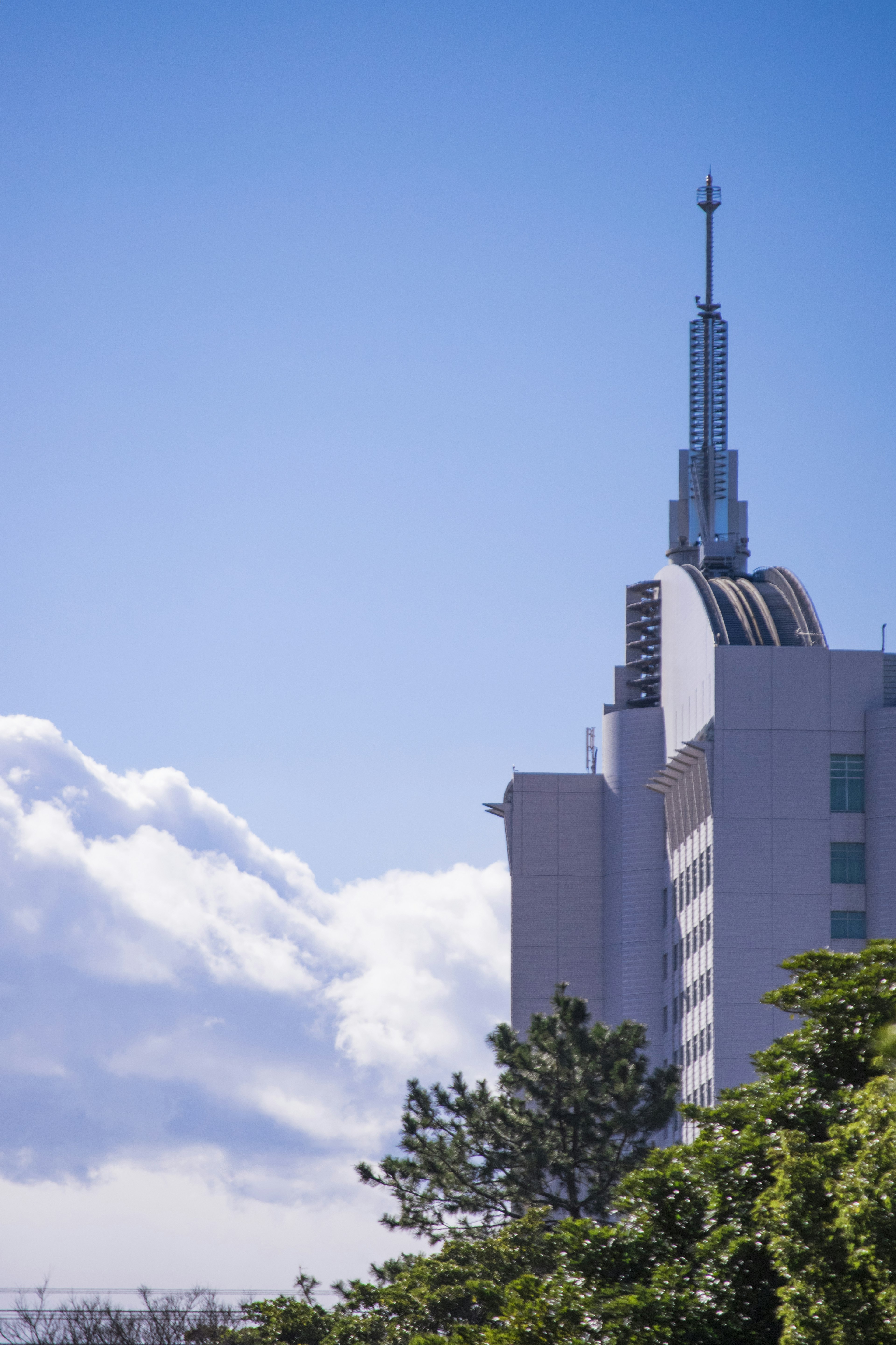 High-rise building spire against a clear blue sky and clouds