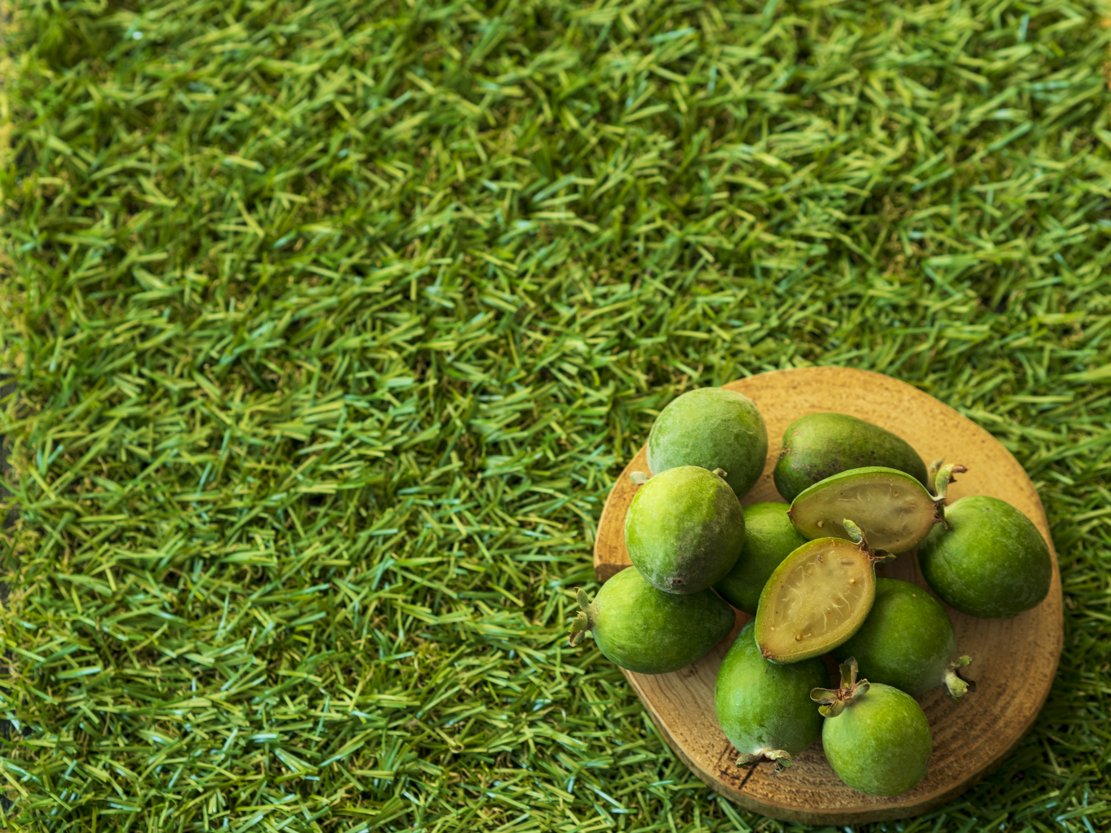 Un bol en bois rempli de fruits verts non mûrs posé sur de l'herbe verte