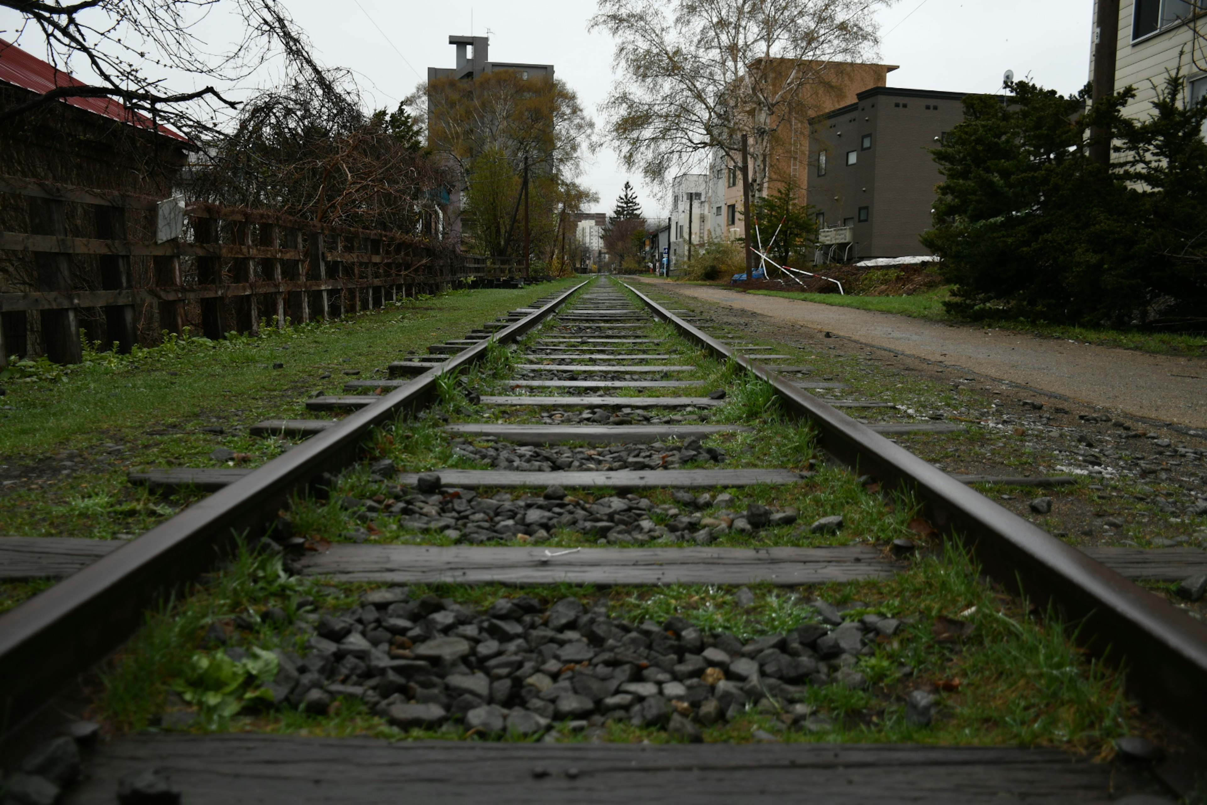 มุมมองของรางรถไฟที่มีหญ้าขึ้นระหว่างรางล้อมรอบด้วยอาคาร