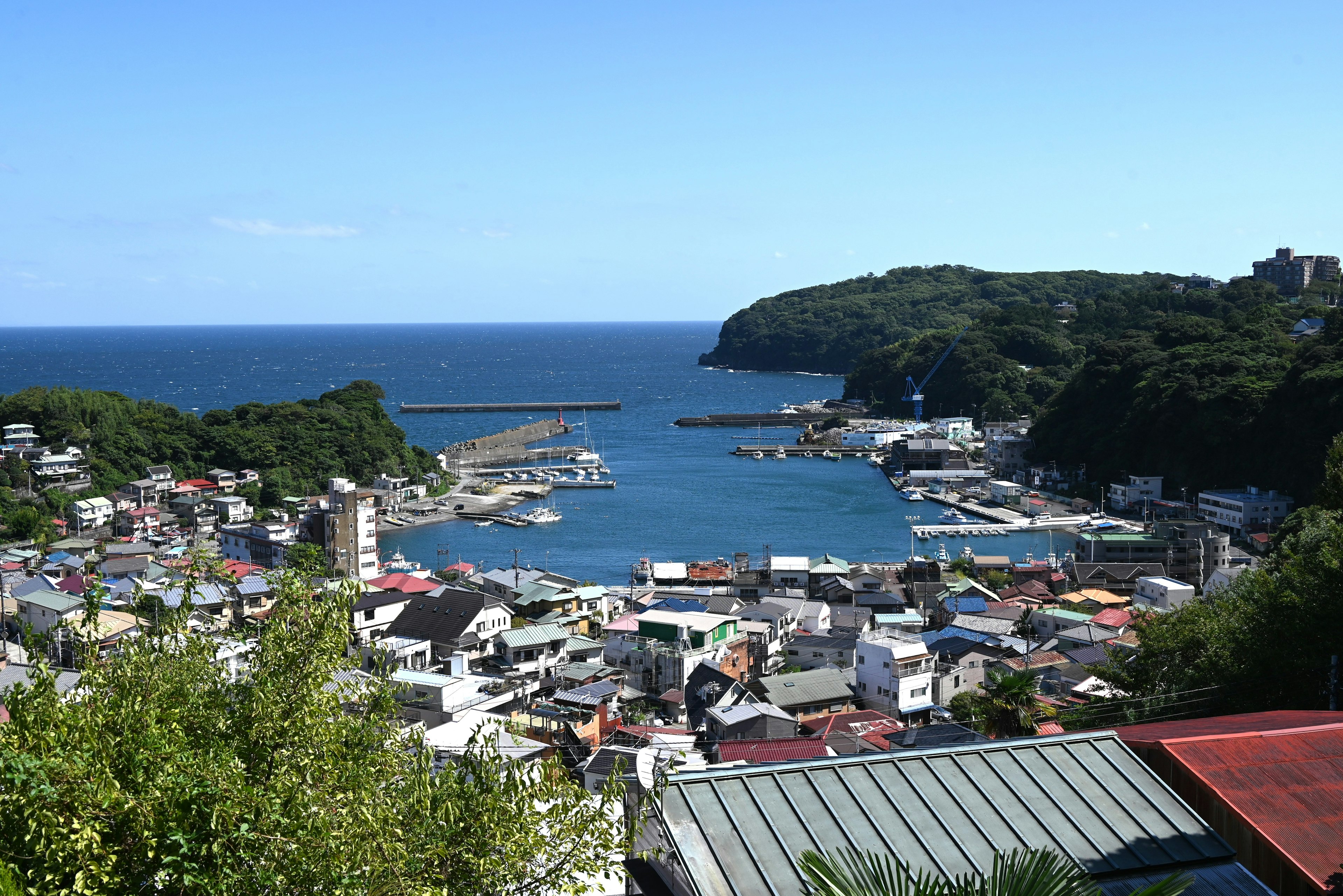 Vue pittoresque d'un port avec des maisons colorées entourées de collines verdoyantes et d'un ciel bleu clair