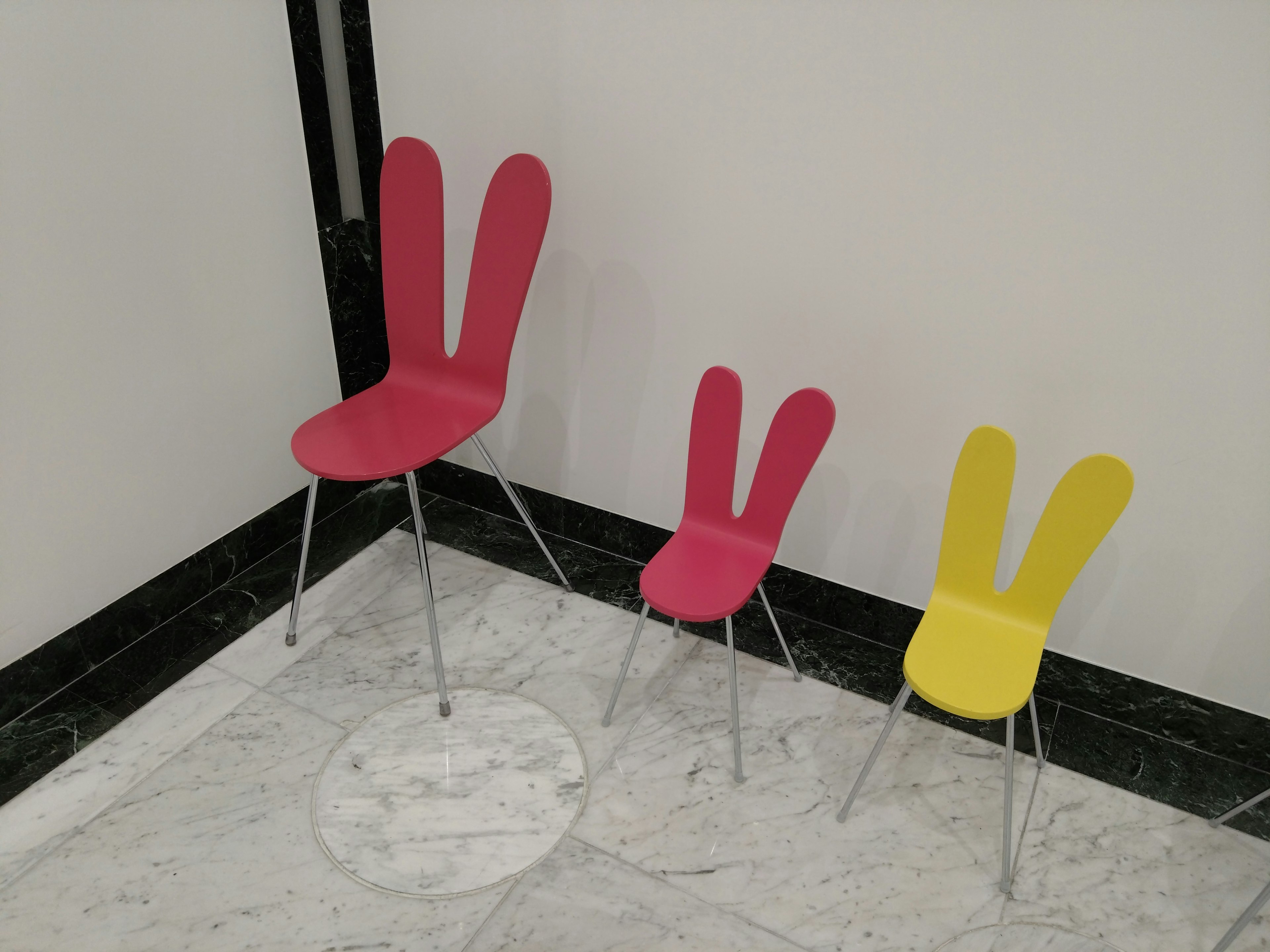 Three colorful rabbit ear chairs in pink and yellow arranged in a row